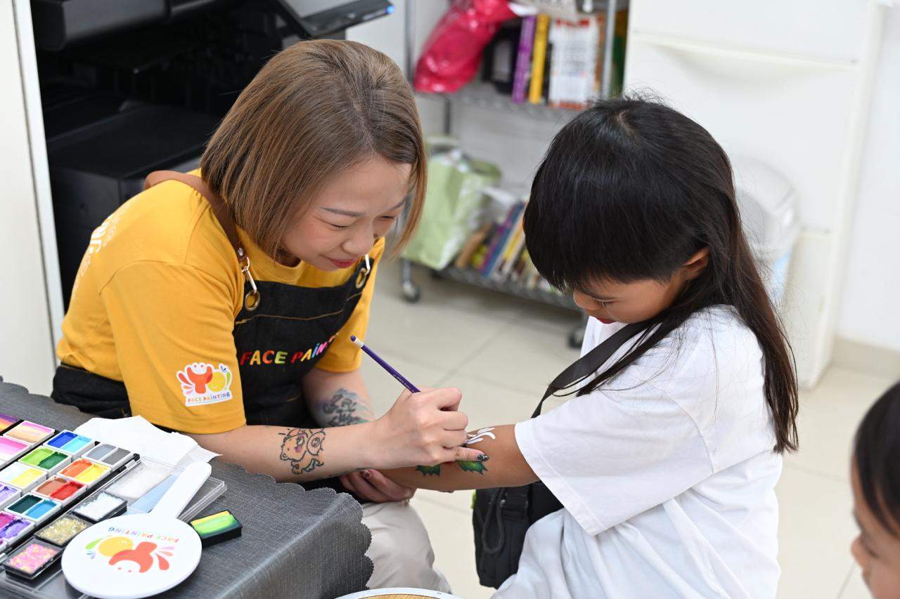 An adult paints a child's hand beside watercolour supplies.