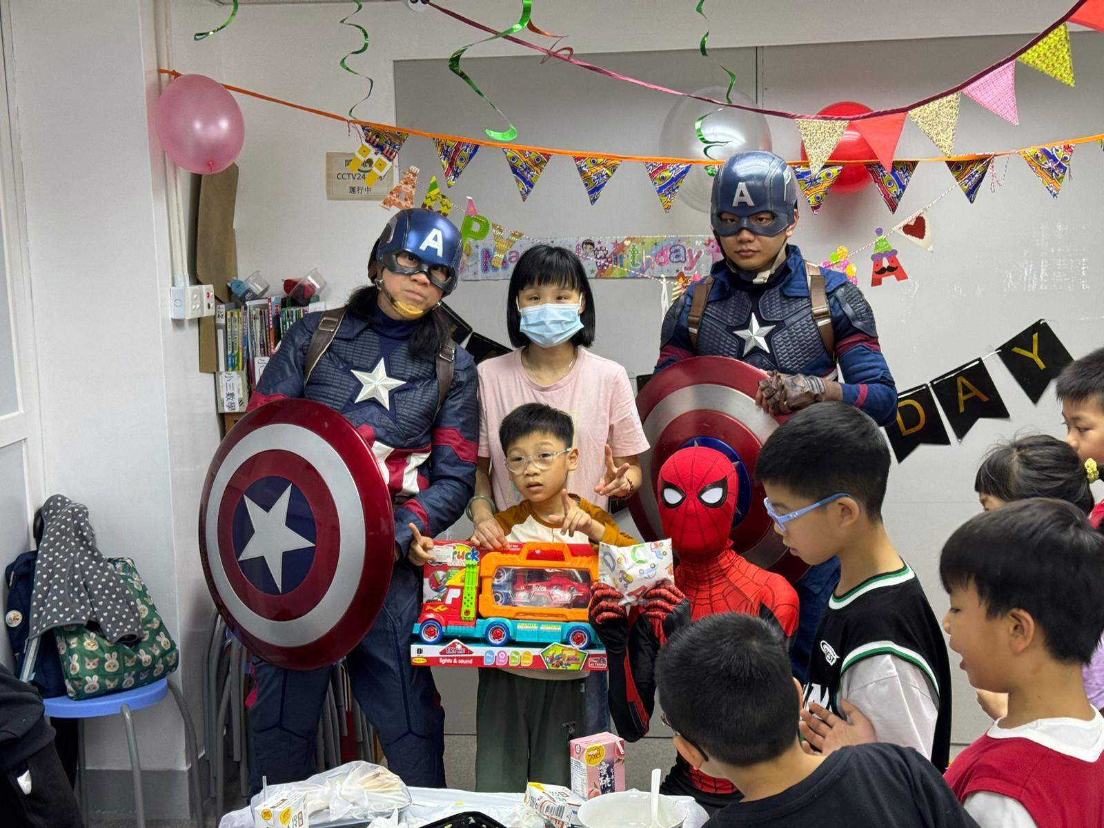 Costumed performers pose with children holding a boxed toy.