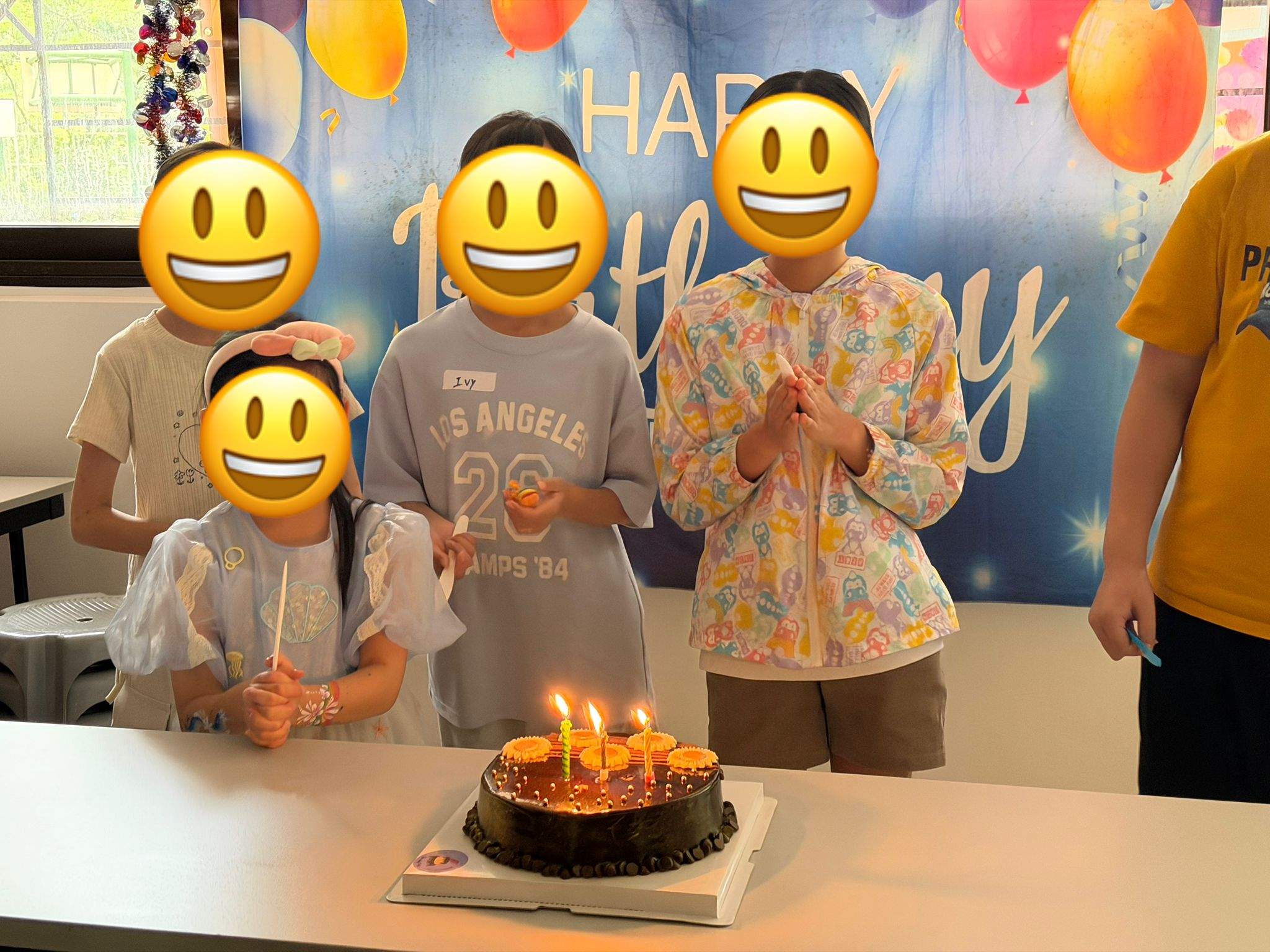 A group gathers behind a candlelit birthday cake.