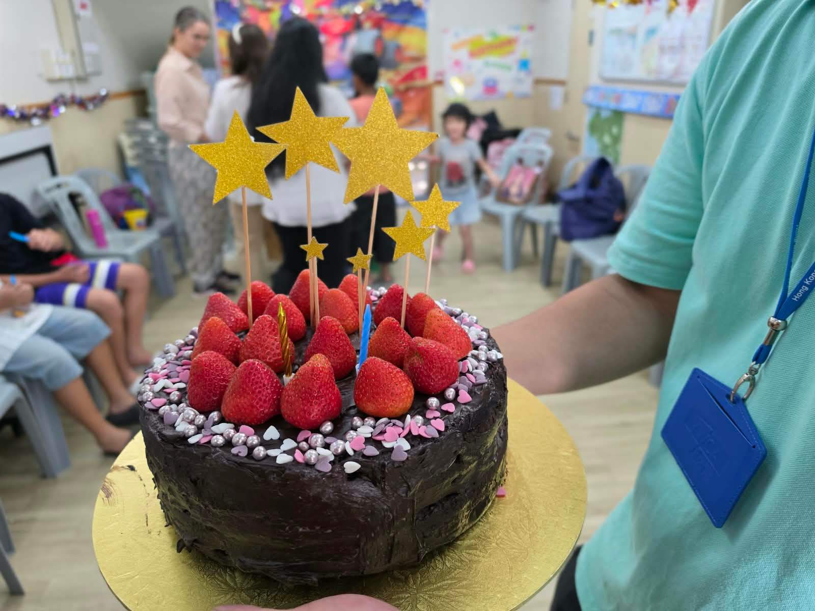 A strawberry-topped chocolate birthday cake is carried into the room.