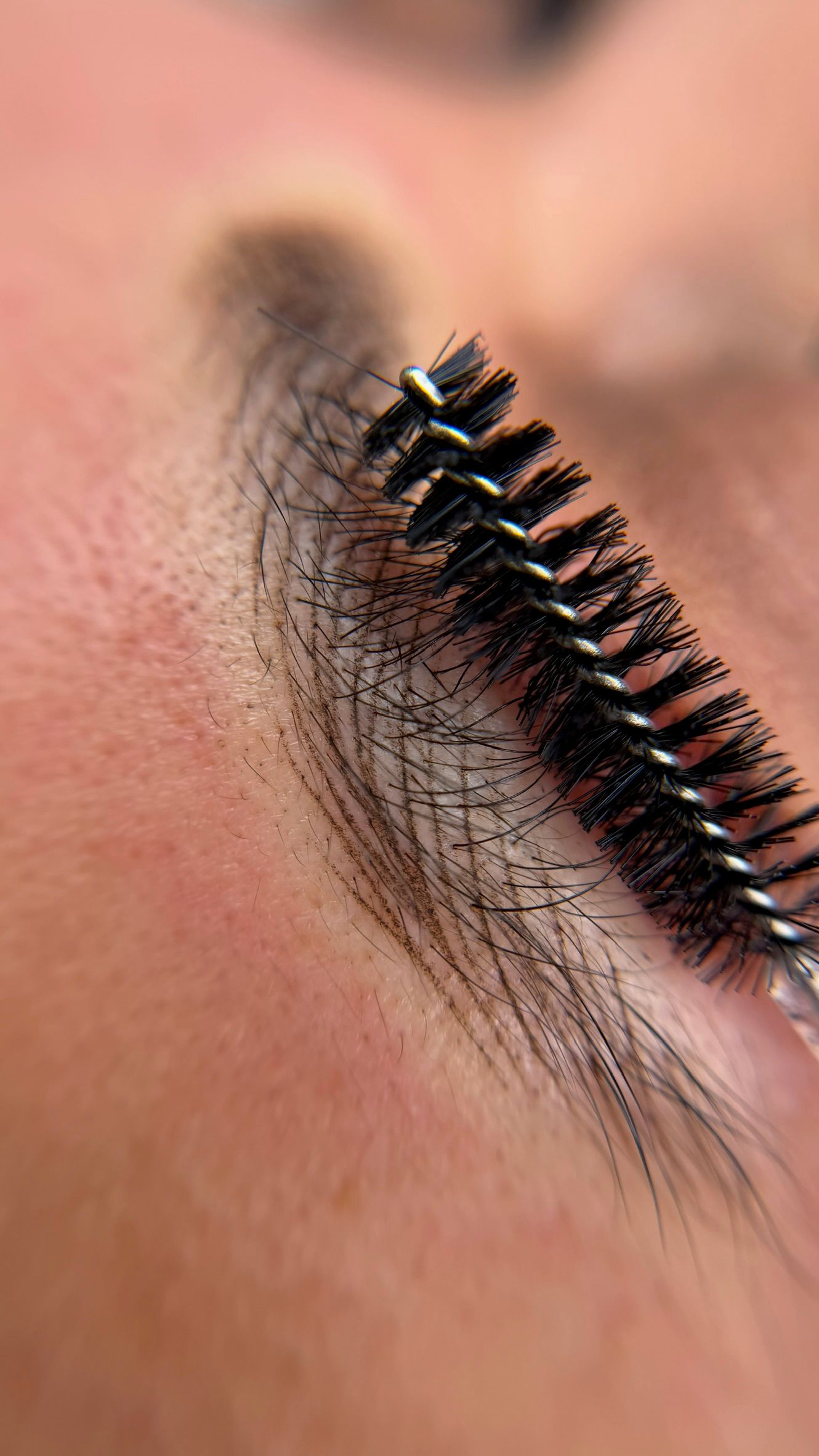 Macro view of a spoolie brush combing through hyper-realistic nano brow strokes to show seamless blending with natural eyebrow hair.