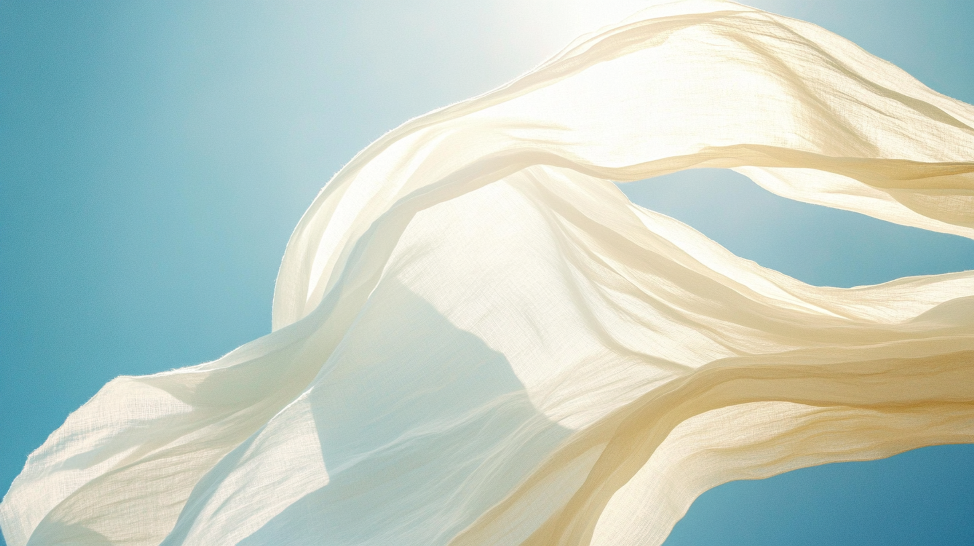 A cinematic, ethereal photograph of light, semi-sheer white linen fabric billowing wildly and freely in a strong breeze against a clear, bright blue sky. The sun catches the texture of the fabric. The image symbolizes freedom, release, and a new beginning.