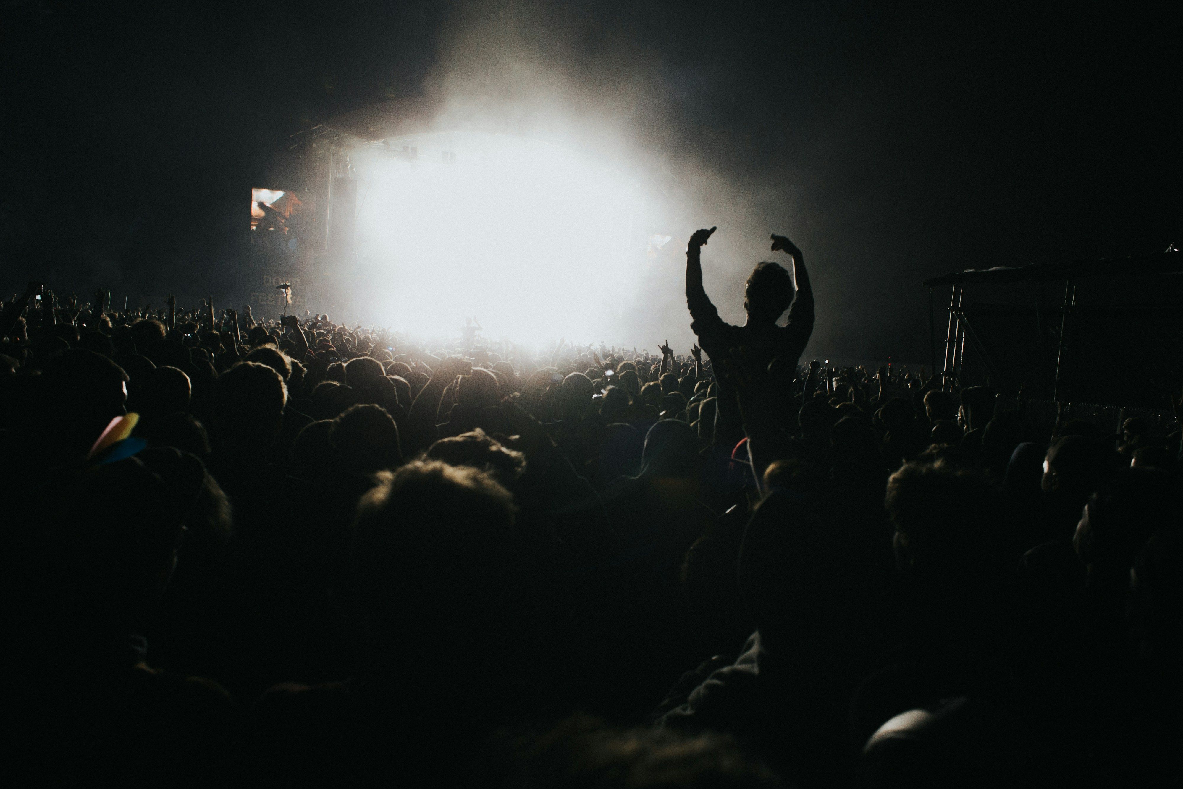 Silhouettes of a music festival crowd in front of a lit stage