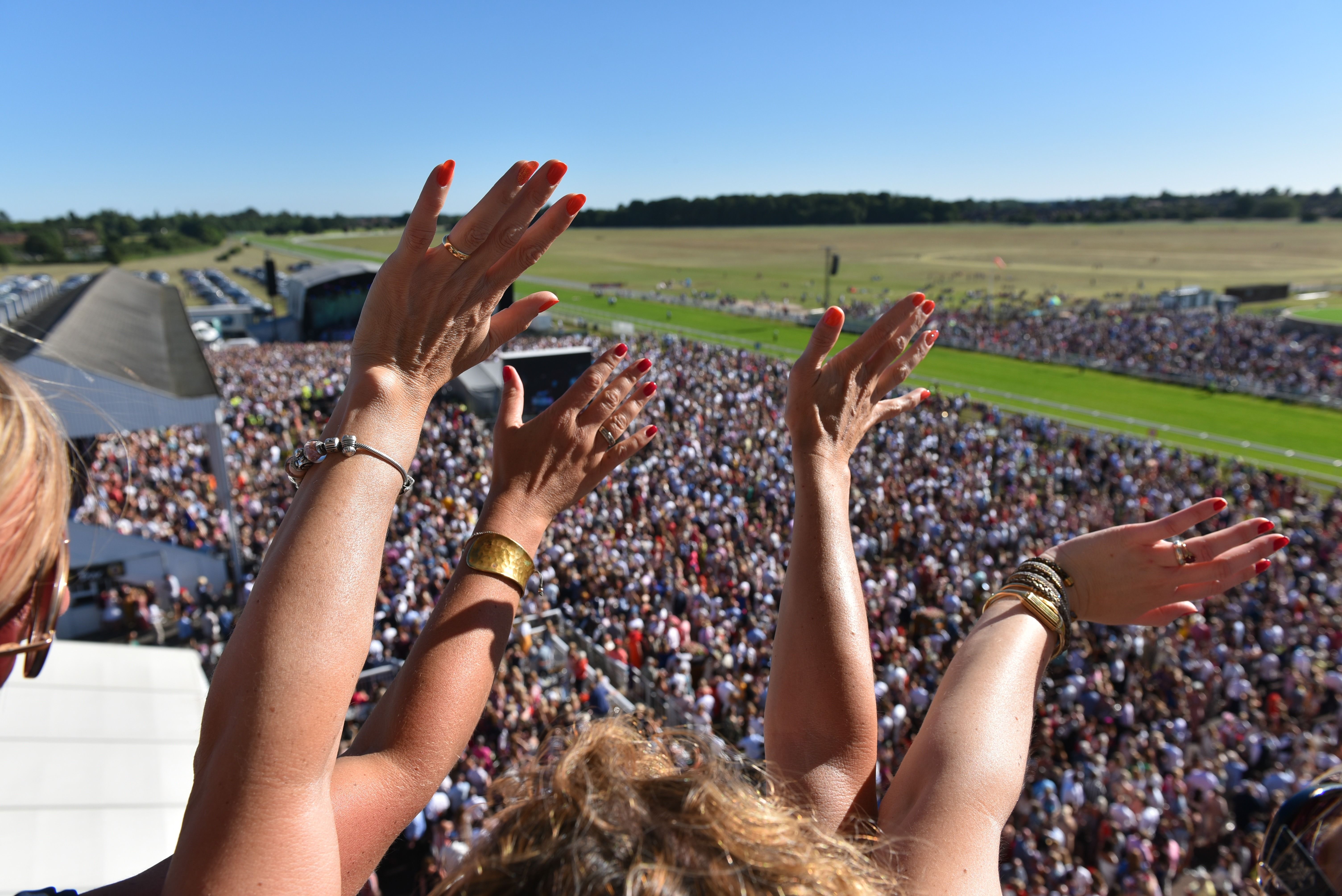 The view down from a balcony at York Racecourse over a large crowd towards the track, with spectators applauding in the foreground
