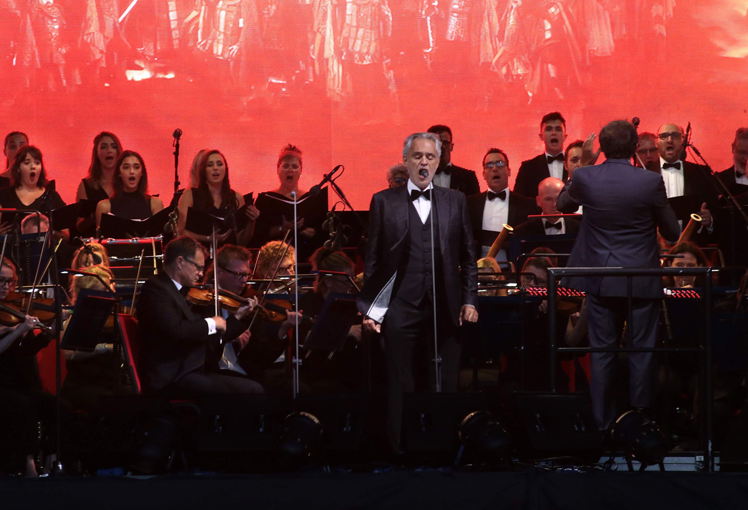Andrea Bocelli on a red-lit stage with orchestra and choir