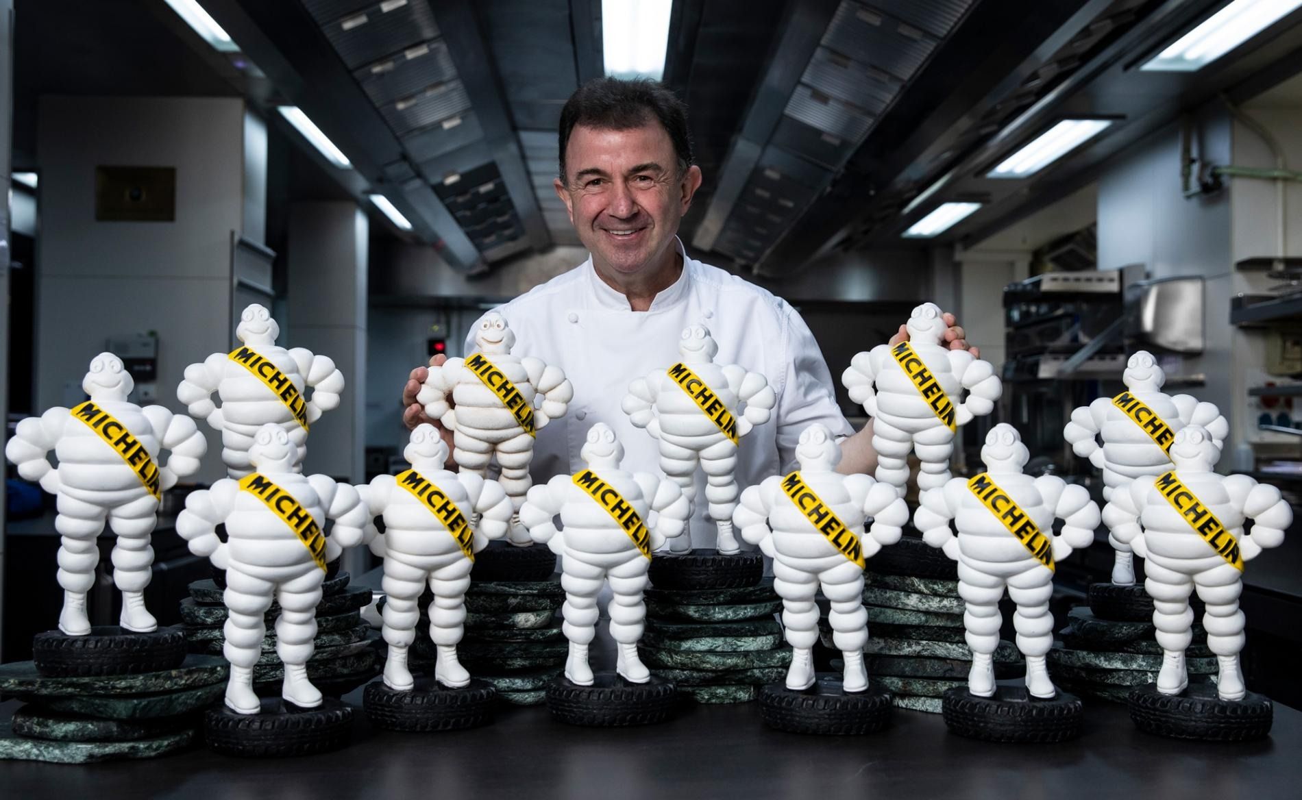 A chef in whites standing behind a row of white Michelin Man figures in a restaurant kitchen