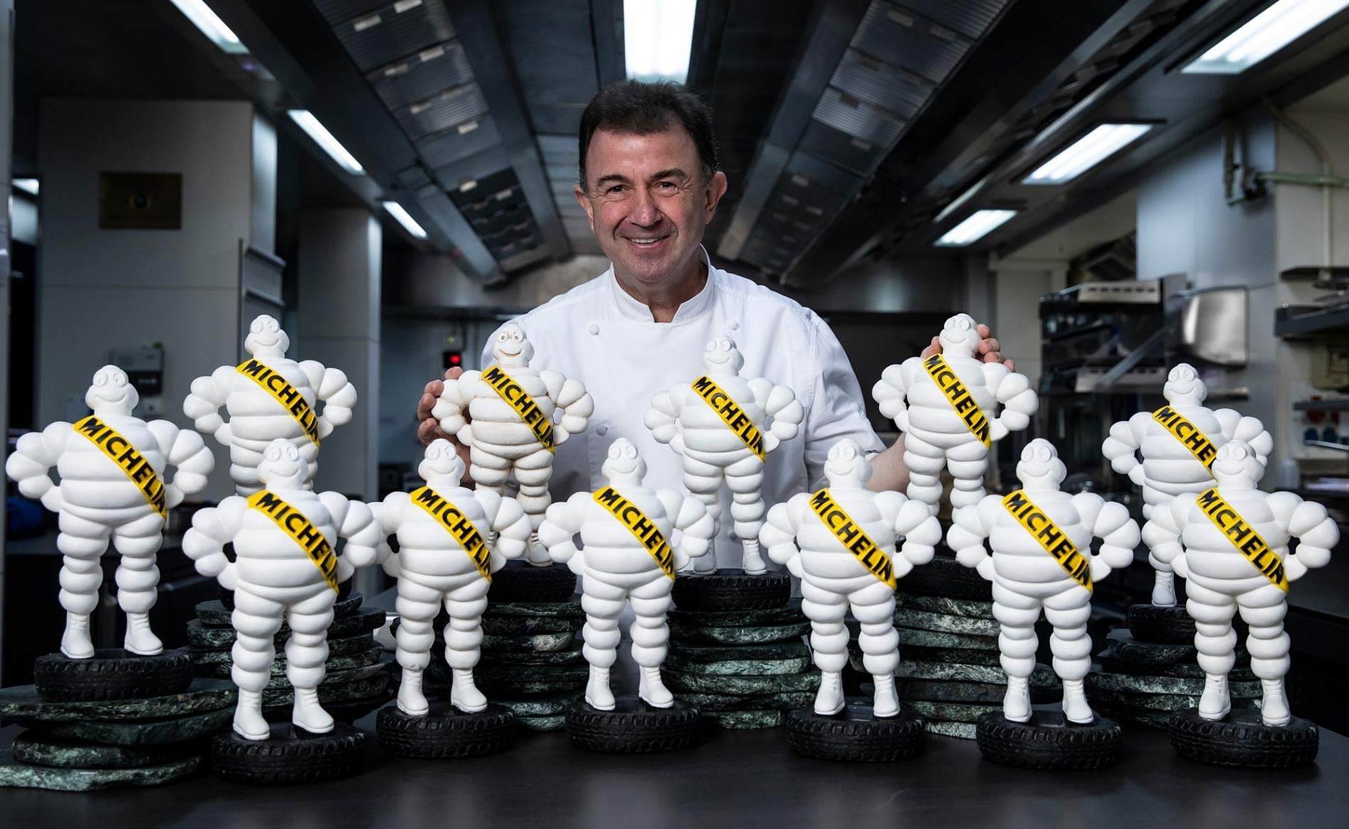 A chef in whites standing behind a row of white Michelin Man figures in a restaurant kitchen