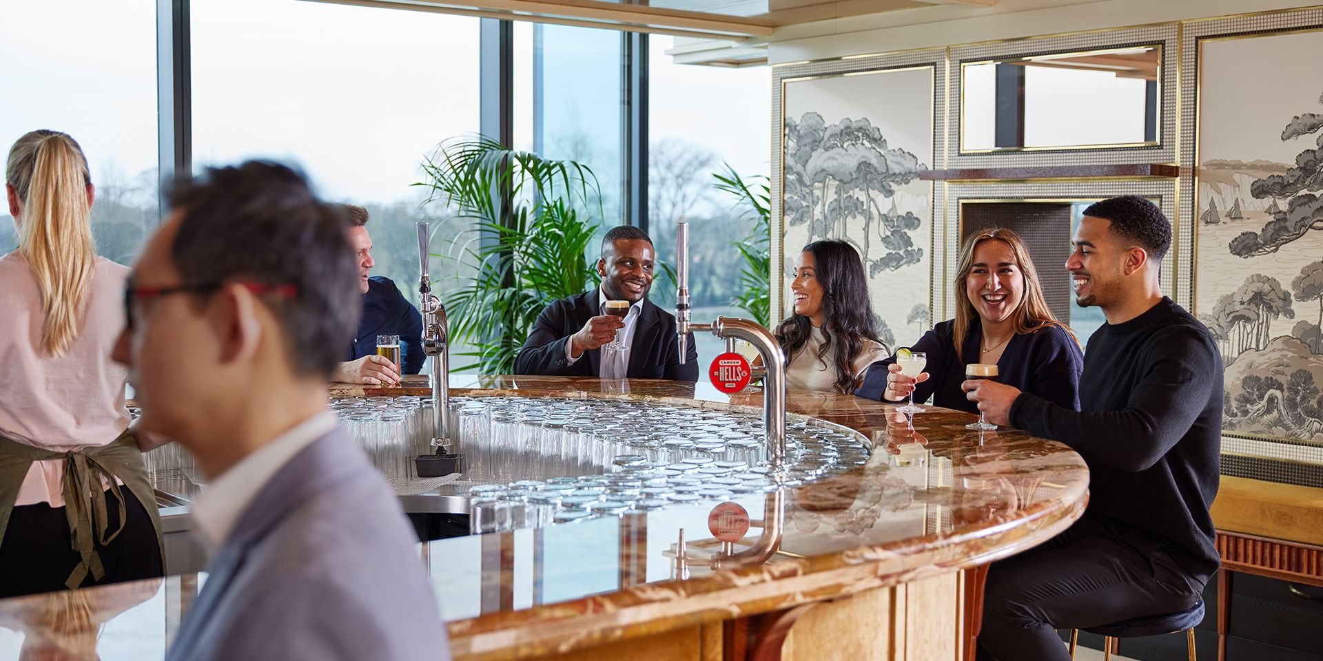 Guests at the curved marble bar of The Sky Deck beside the riverside windows