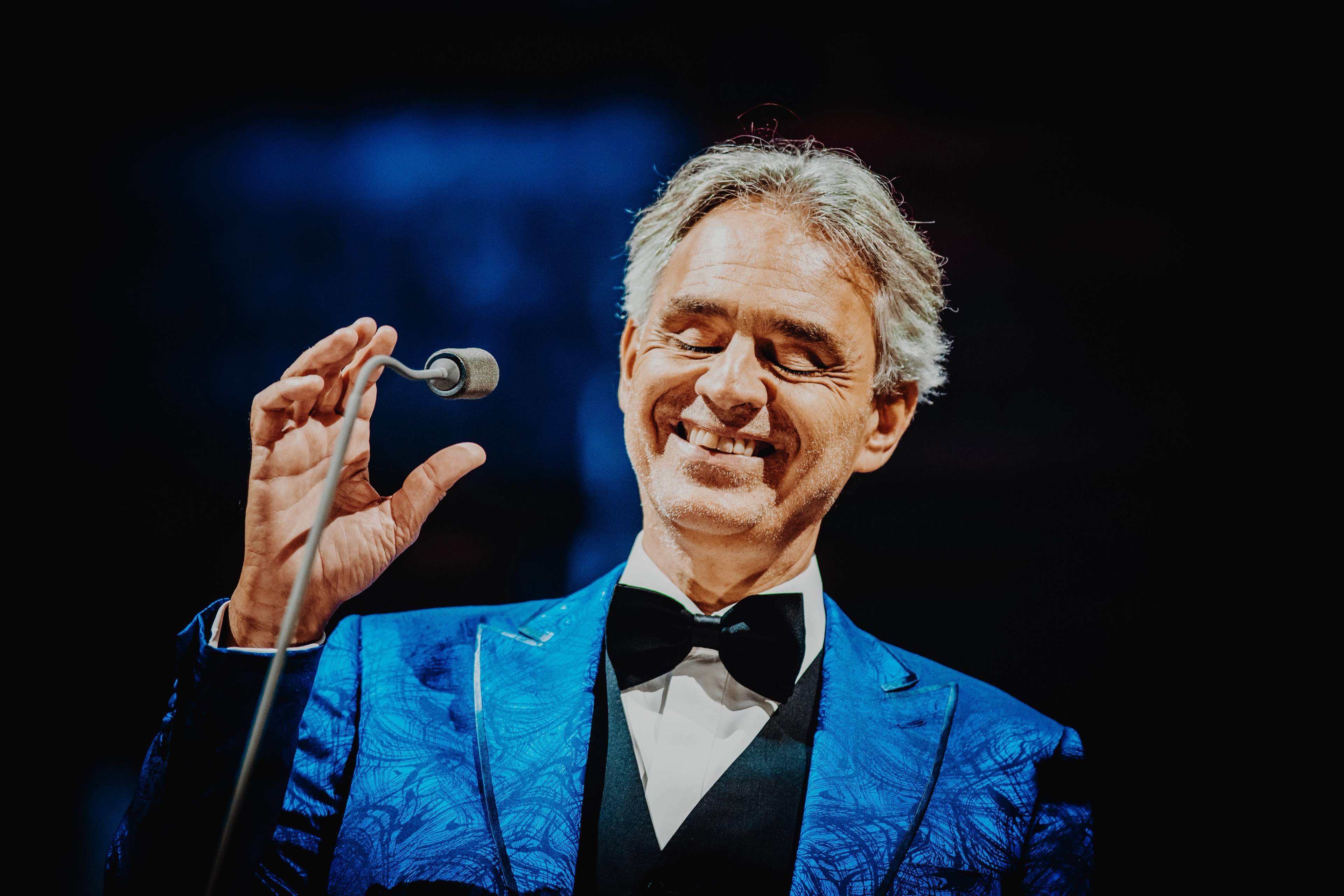 Andrea Bocelli smiling at the microphone in a blue jacket