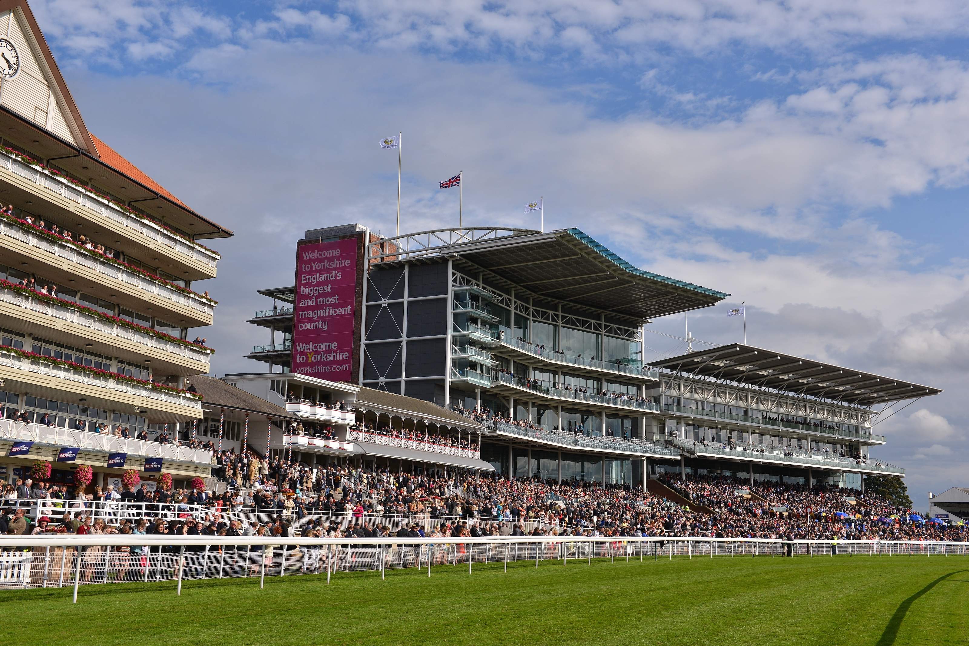 The tiered grandstands at York Racecourse seen from the track, with balconies running across several floors above a packed lawn