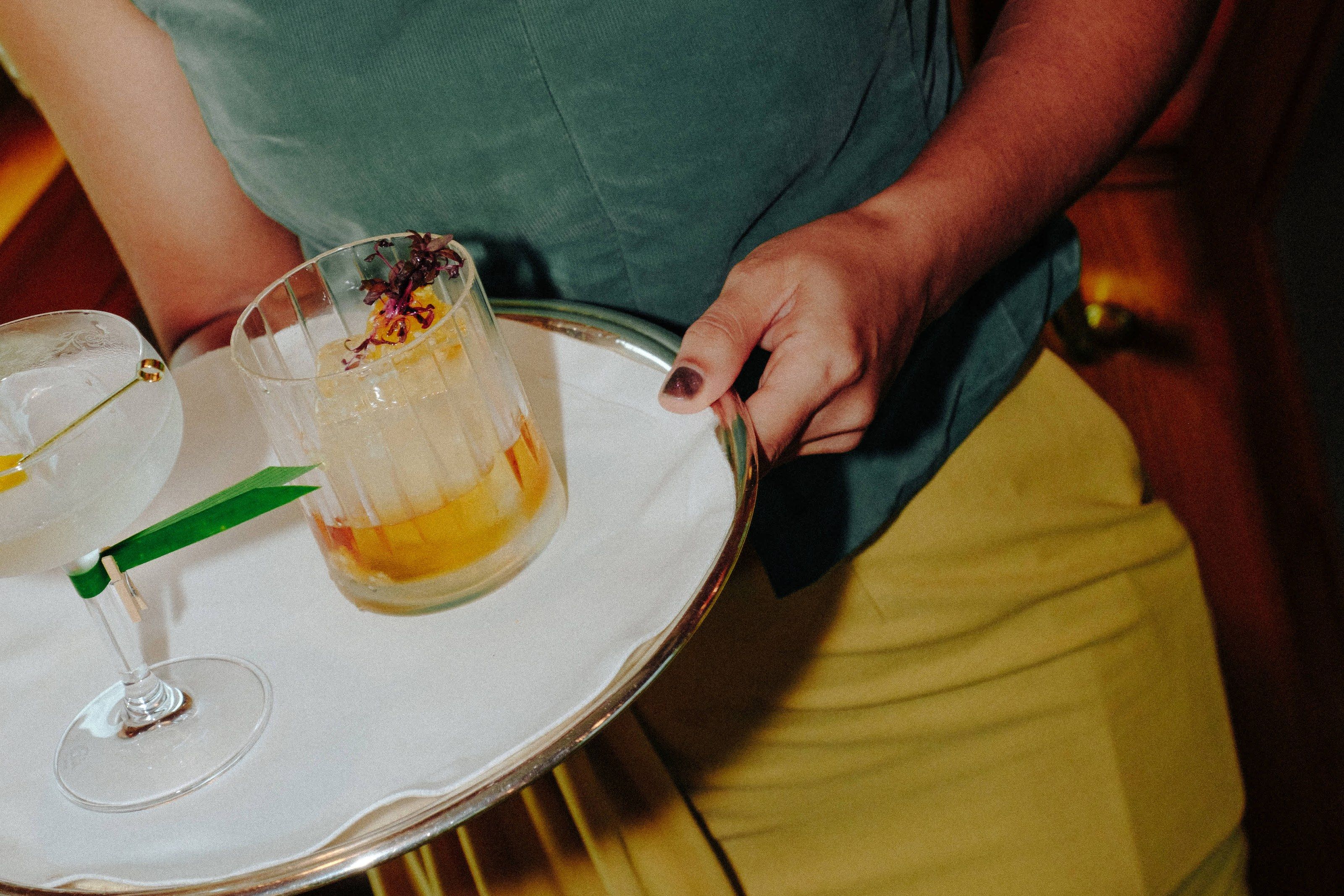 A server carrying a silver tray of cocktails through the piano bar car.