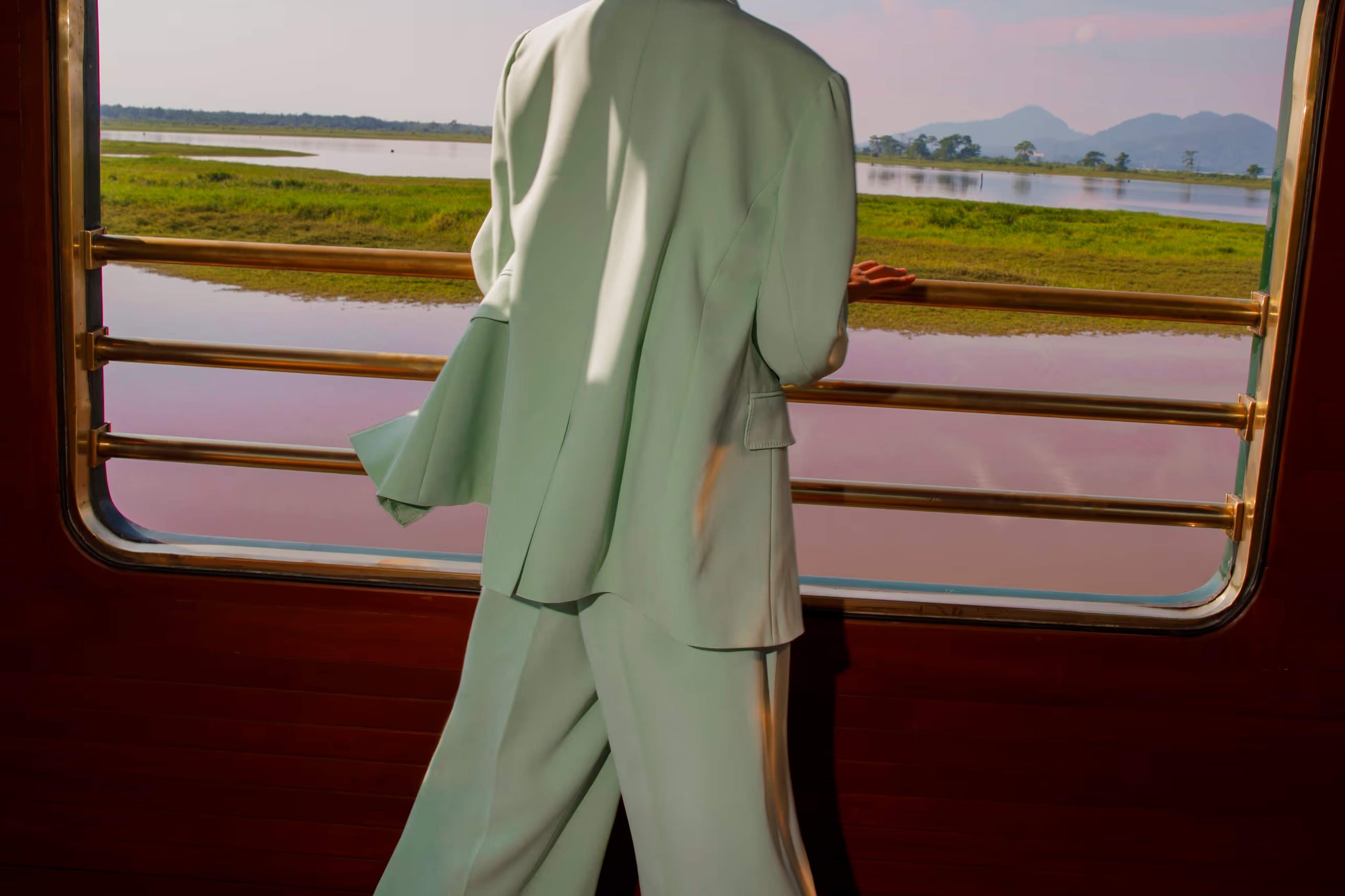 A guest at an open observation-car window of the Eastern & Oriental Express, looking out over Malaysian wetlands and distant hills.