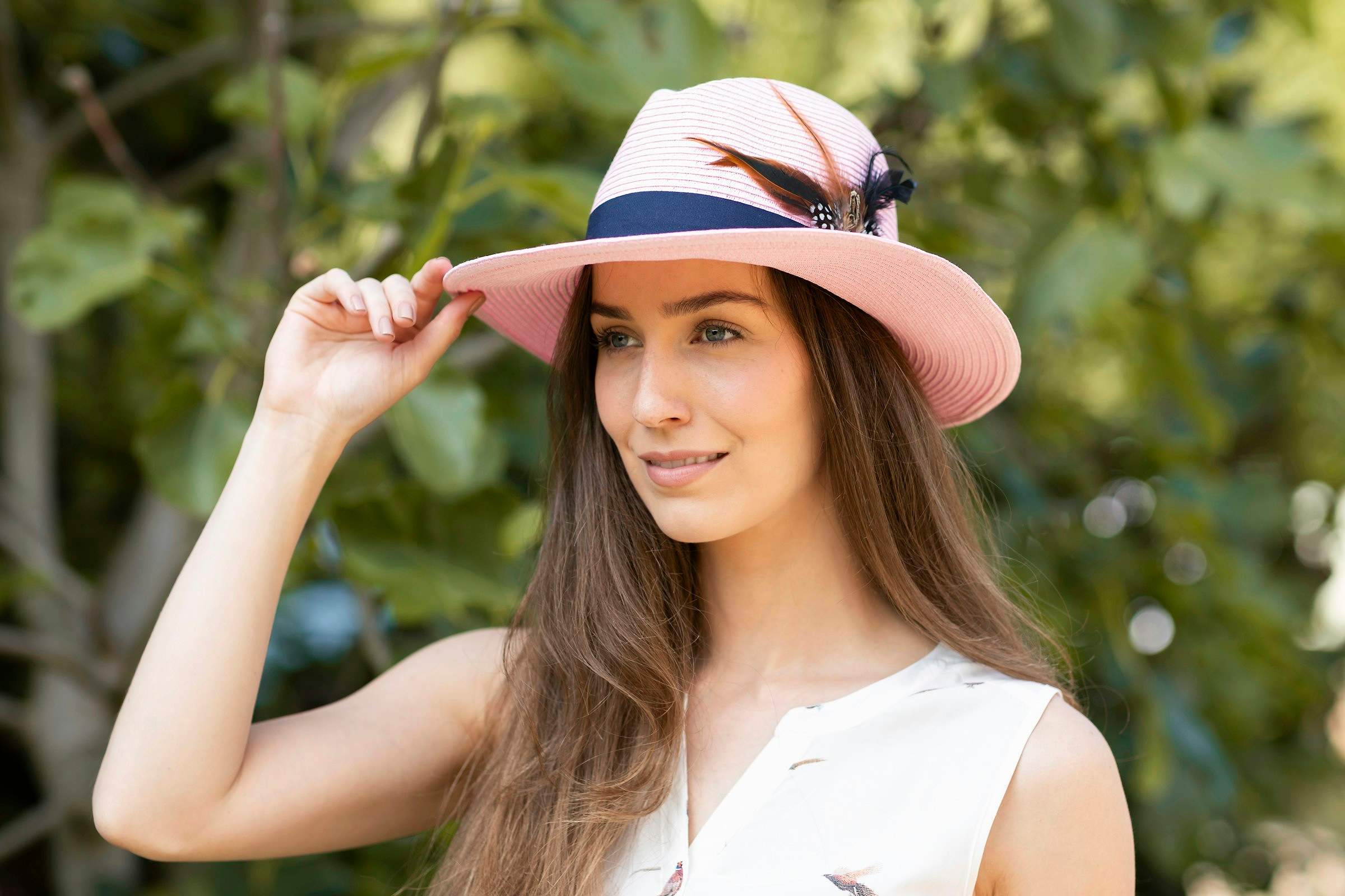 A woman in a pink wide-brim summer hat with a feather trim