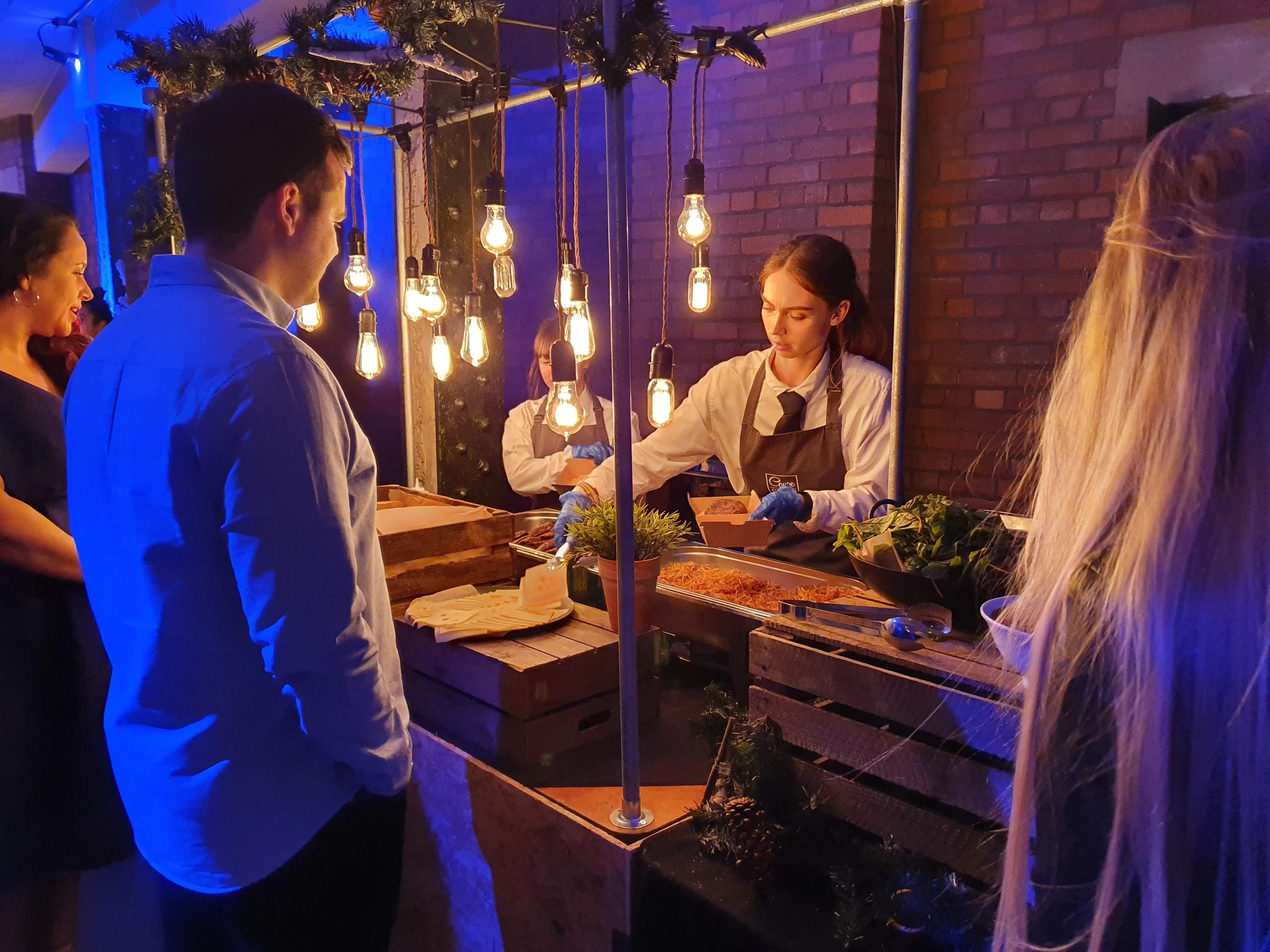 Staff serving food from a wooden station strung with Edison bulbs against exposed brick at Victoria Warehouse, Old Trafford