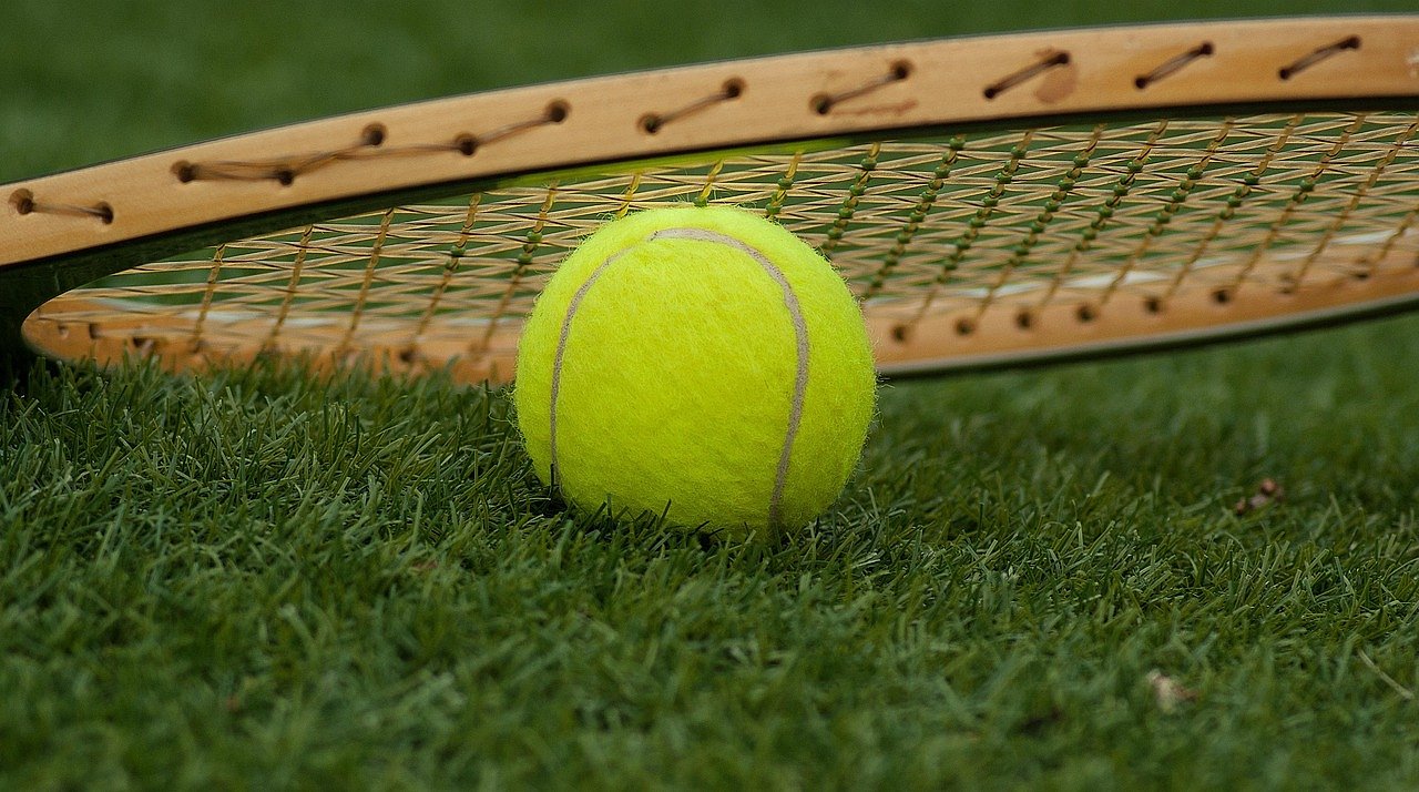 Tennis ball and racket on green court surface, representing the early years of Queen's Club tennis
