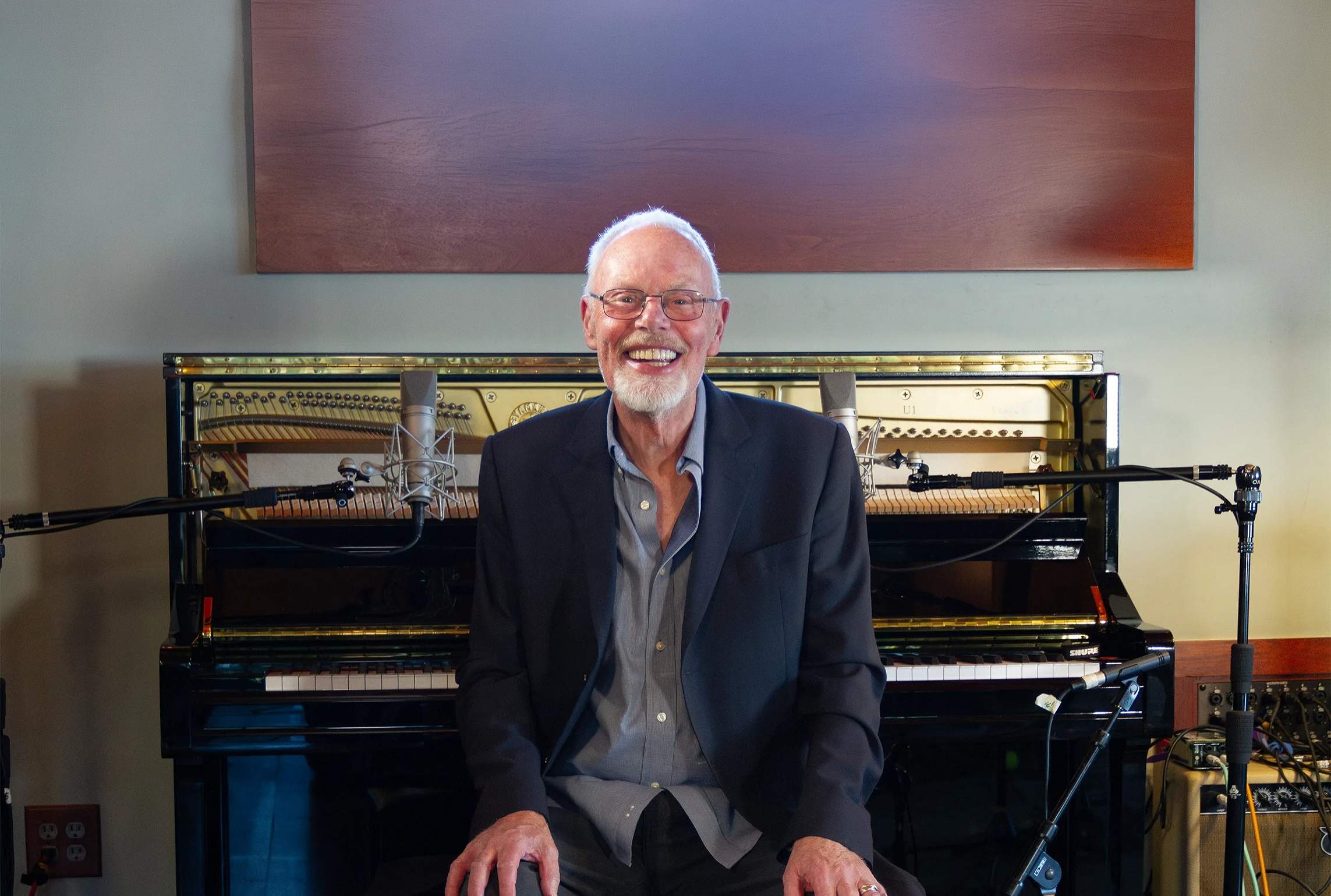 Bob Harris smiling at an upright piano in a recording studio, with microphones set up around it