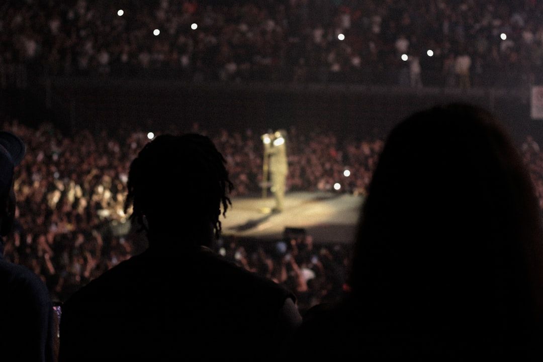 Performer on stage in front of a large arena audience with dramatic lighting
