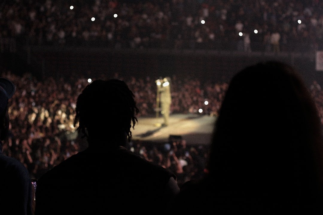 Performer on stage in front of a large arena audience with dramatic lighting