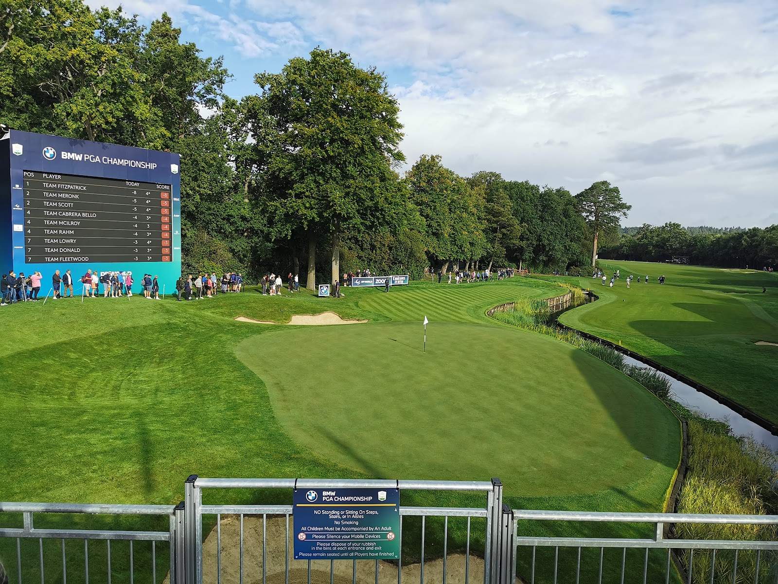Wentworth's 18th green beside the water, with a Pro-Am team leaderboard beyond it