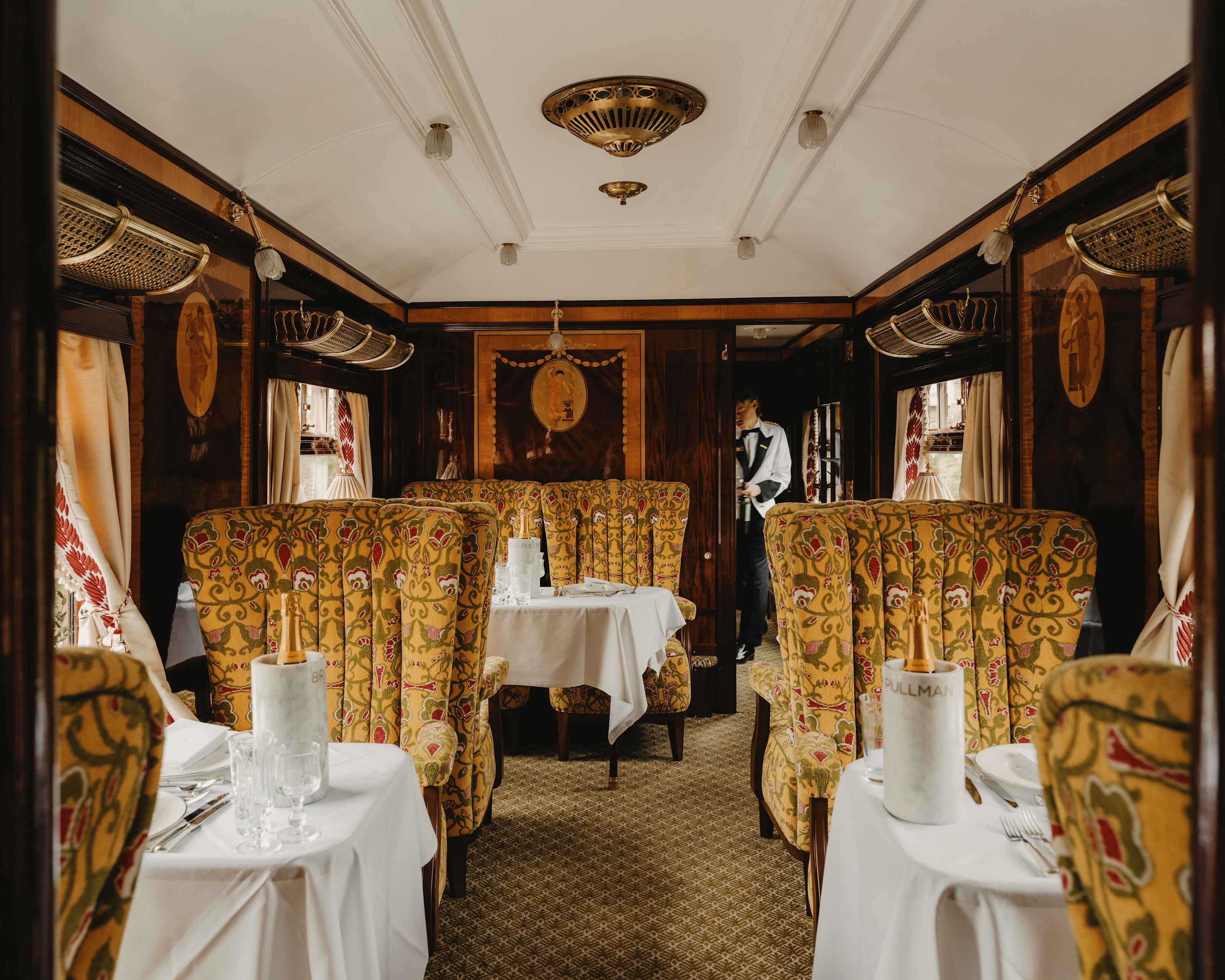Carriage interior with gold patterned armchairs and a steward at the far end