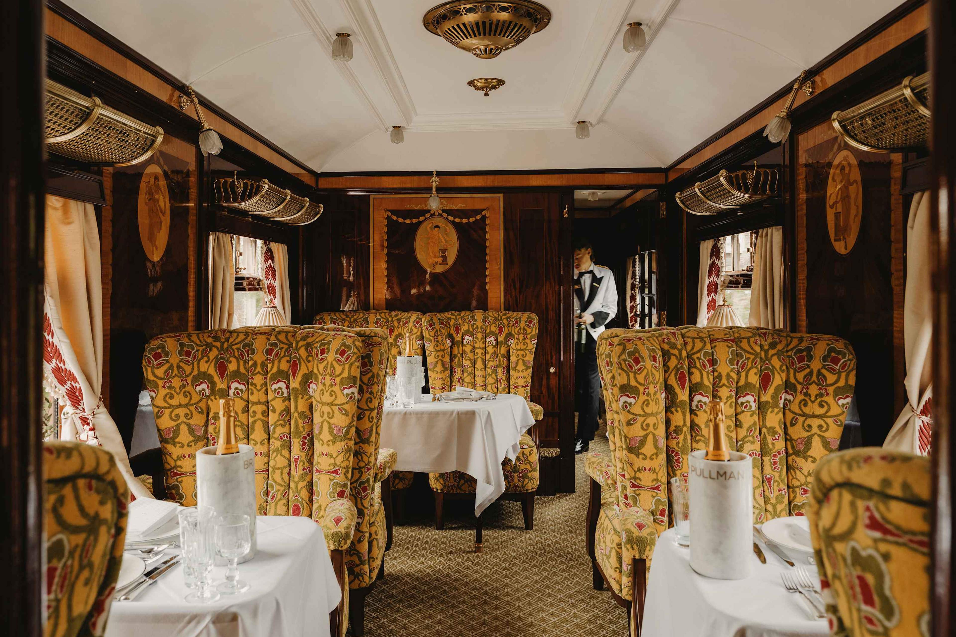 Carriage interior with gold patterned armchairs and a steward at the far end