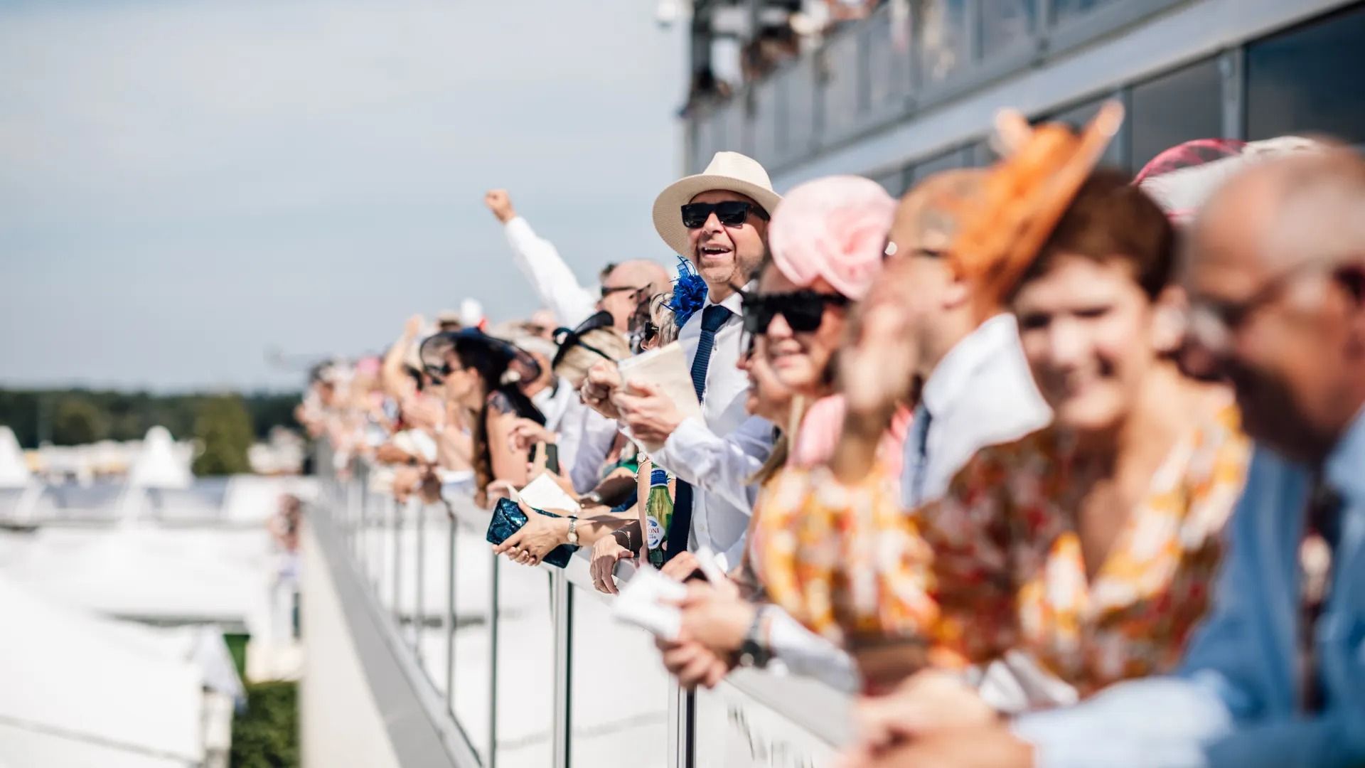 Ladies in colourful hats and summer dresses watching the racing at Royal Ascot
