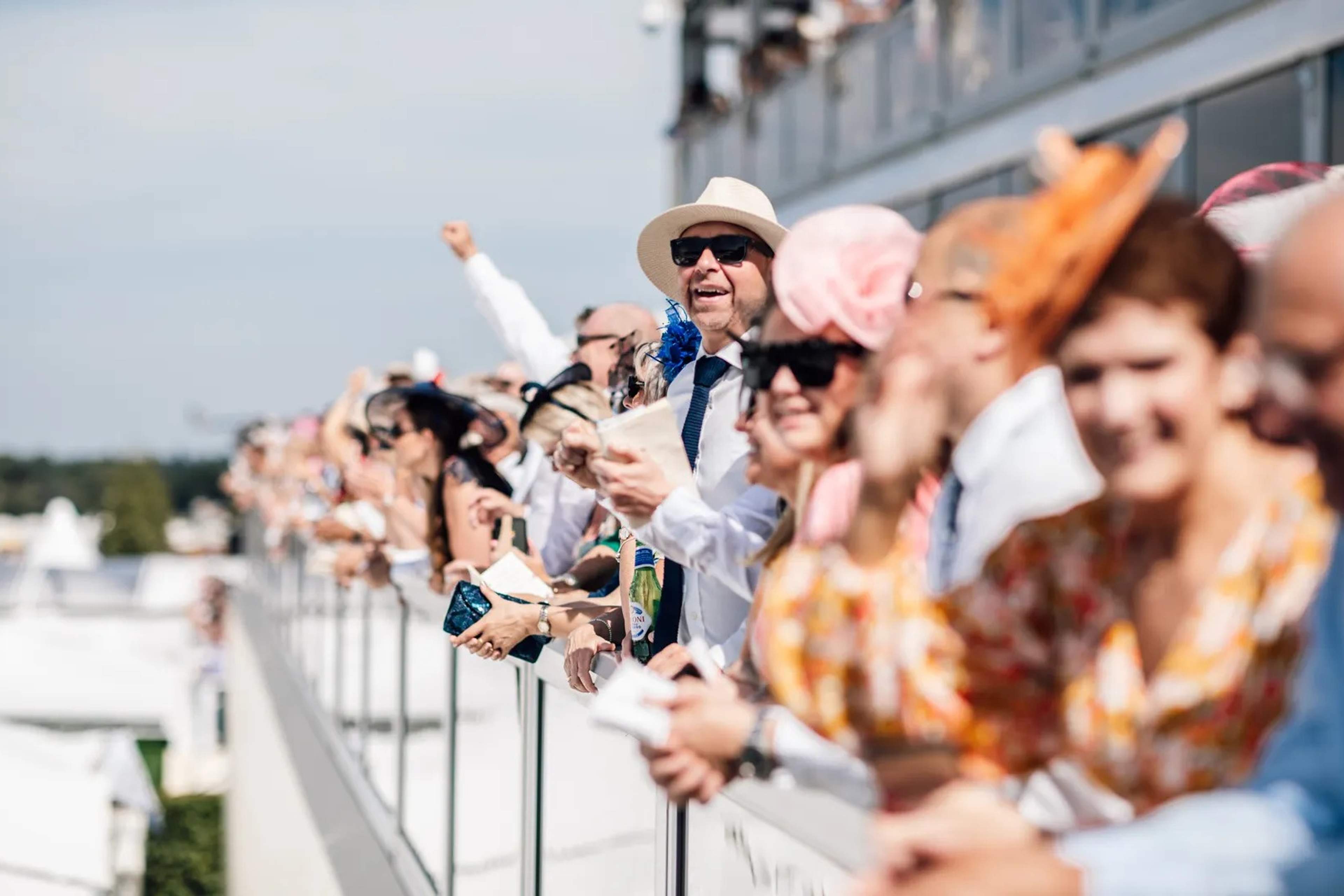 Ladies in colourful hats and summer dresses watching the racing at Royal Ascot