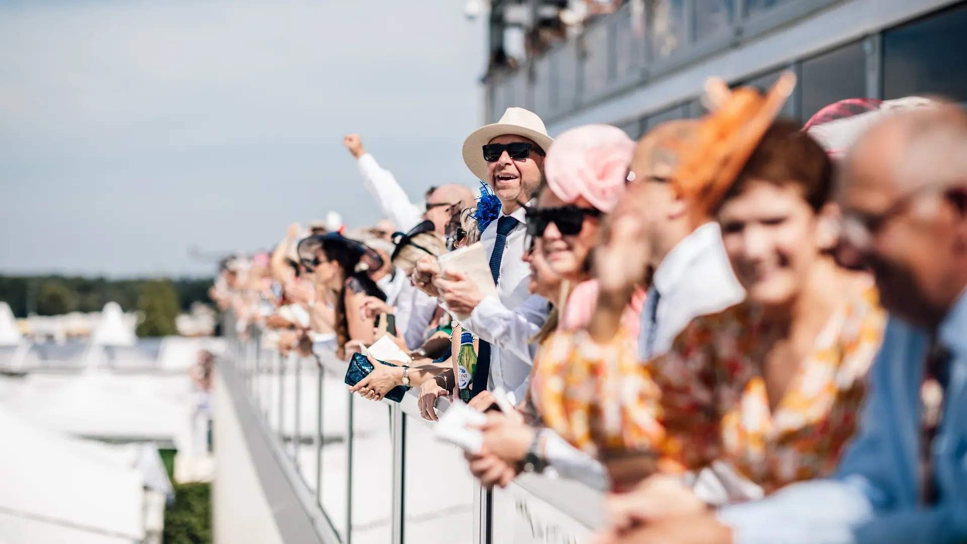 Ladies in colourful hats and summer dresses watching the racing at Royal Ascot