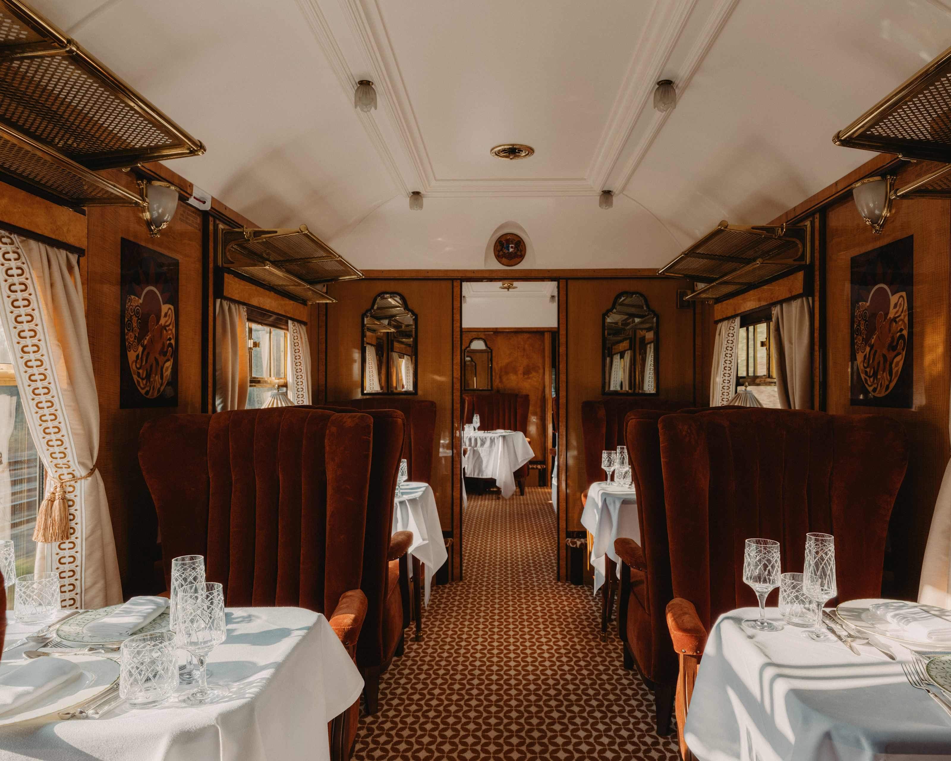 Wood-panelled carriage interior with velvet armchairs and laid tables