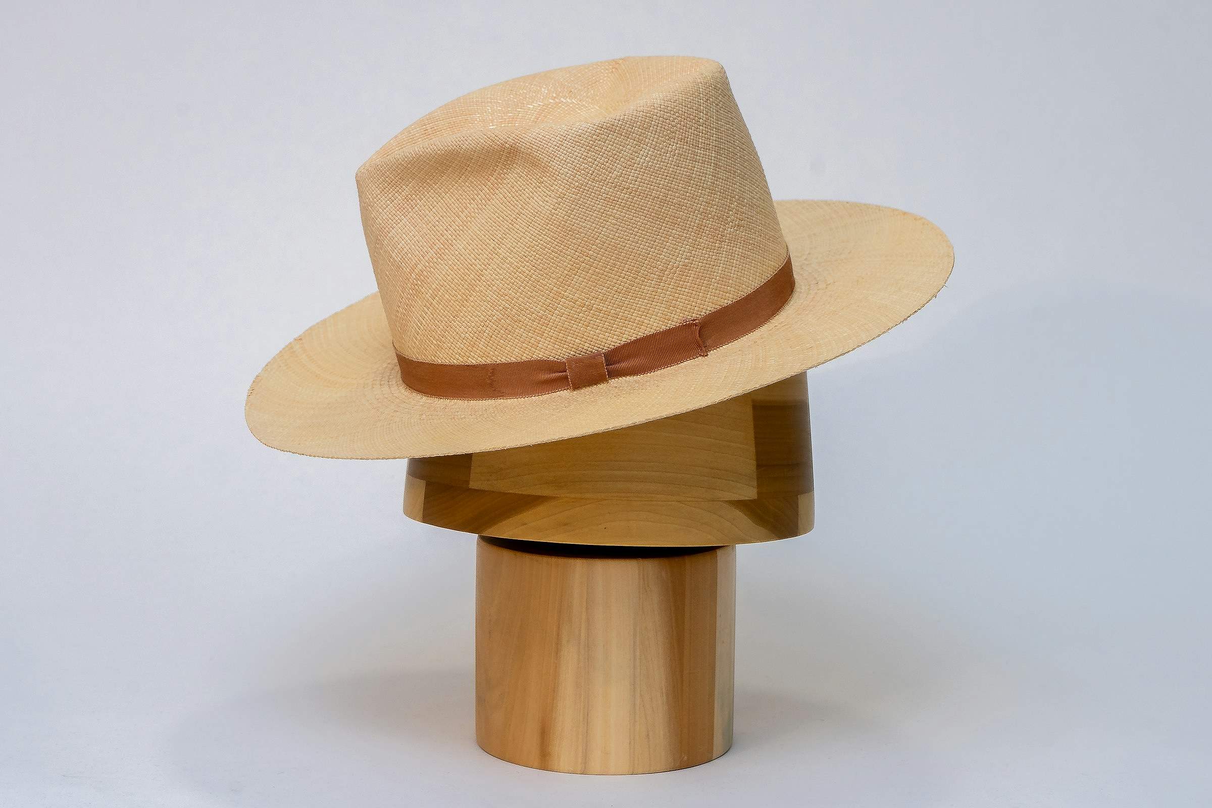 A natural-straw Panama hat with a tan band on a wooden display stand