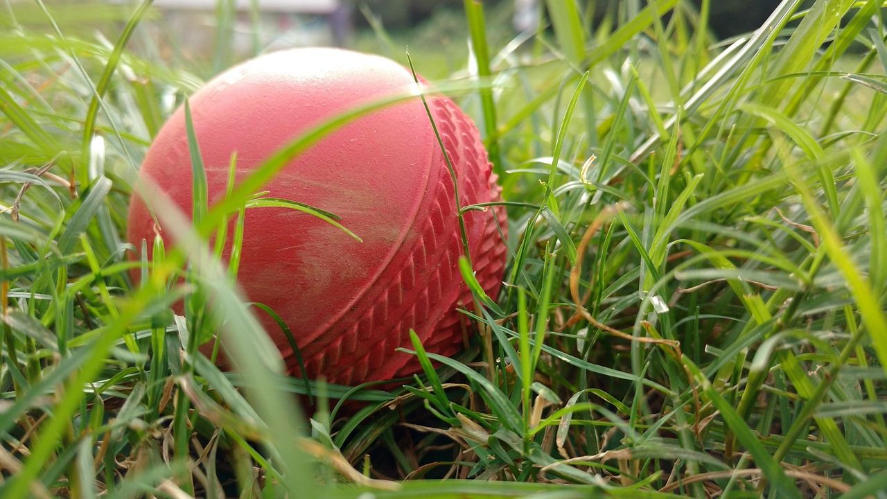 Red cricket ball on green grass, evoking the traditions of Test cricket