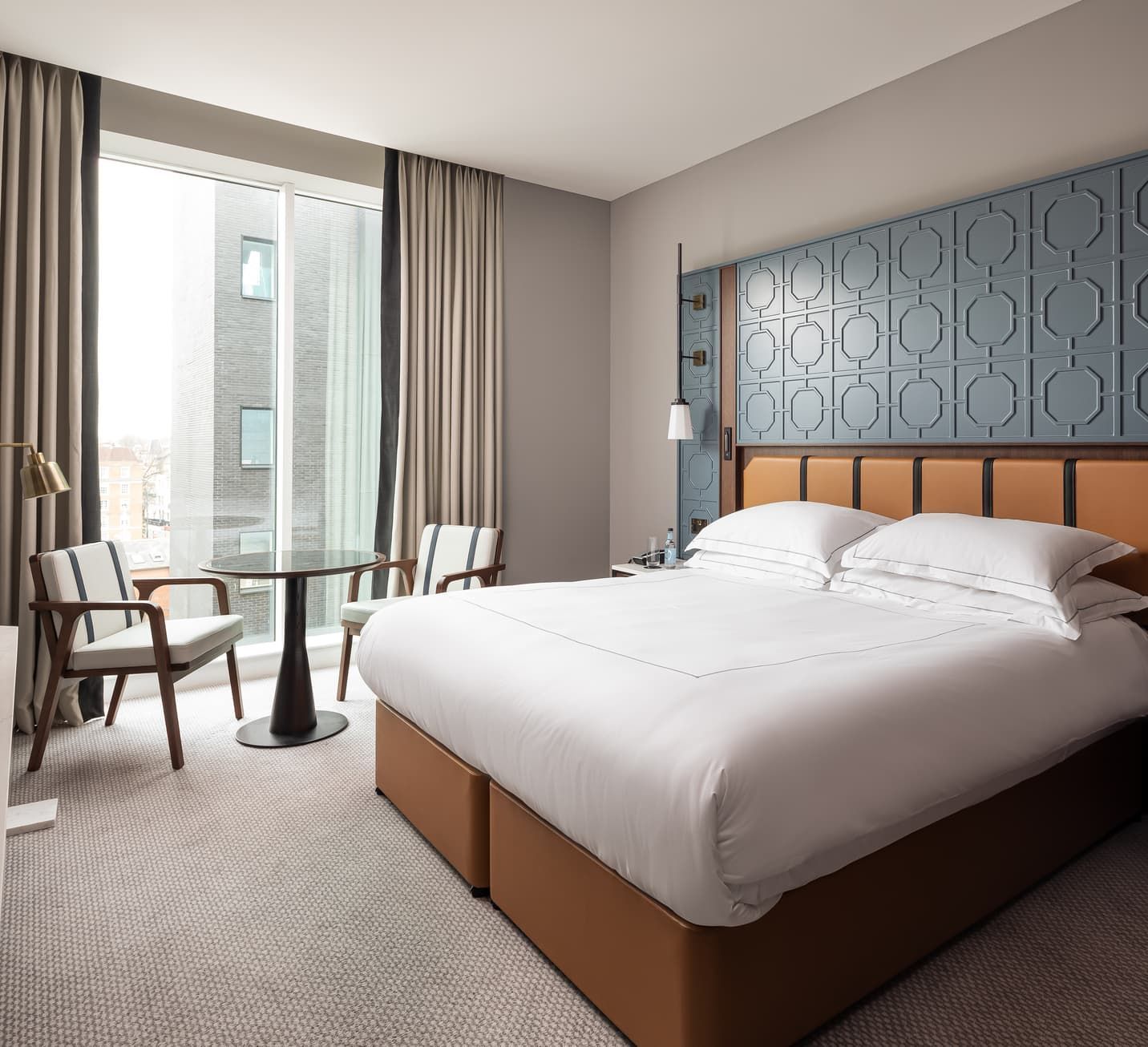 A hotel bedroom with a king bed, dark wood panelling and a seating area by the window