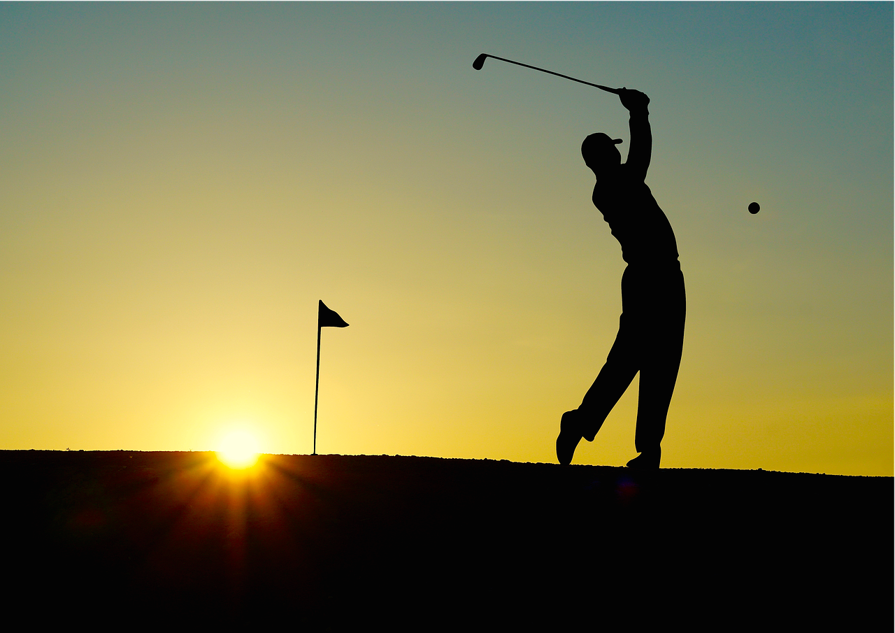 Golfer silhouetted against a sunset on the course