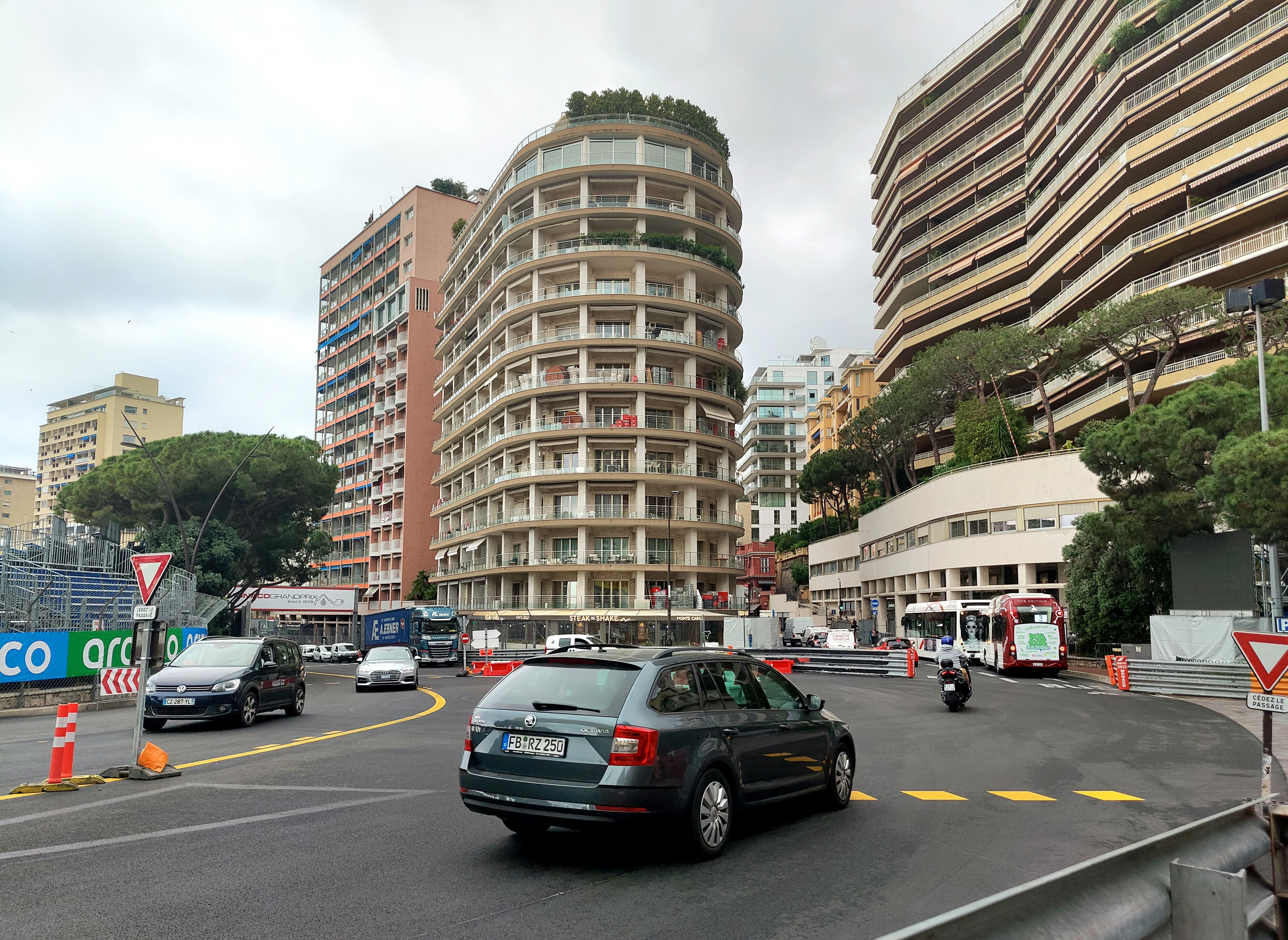 Cars and a bus driving round the Sainte-Dévote corner in Monaco, with the race barriers already in place