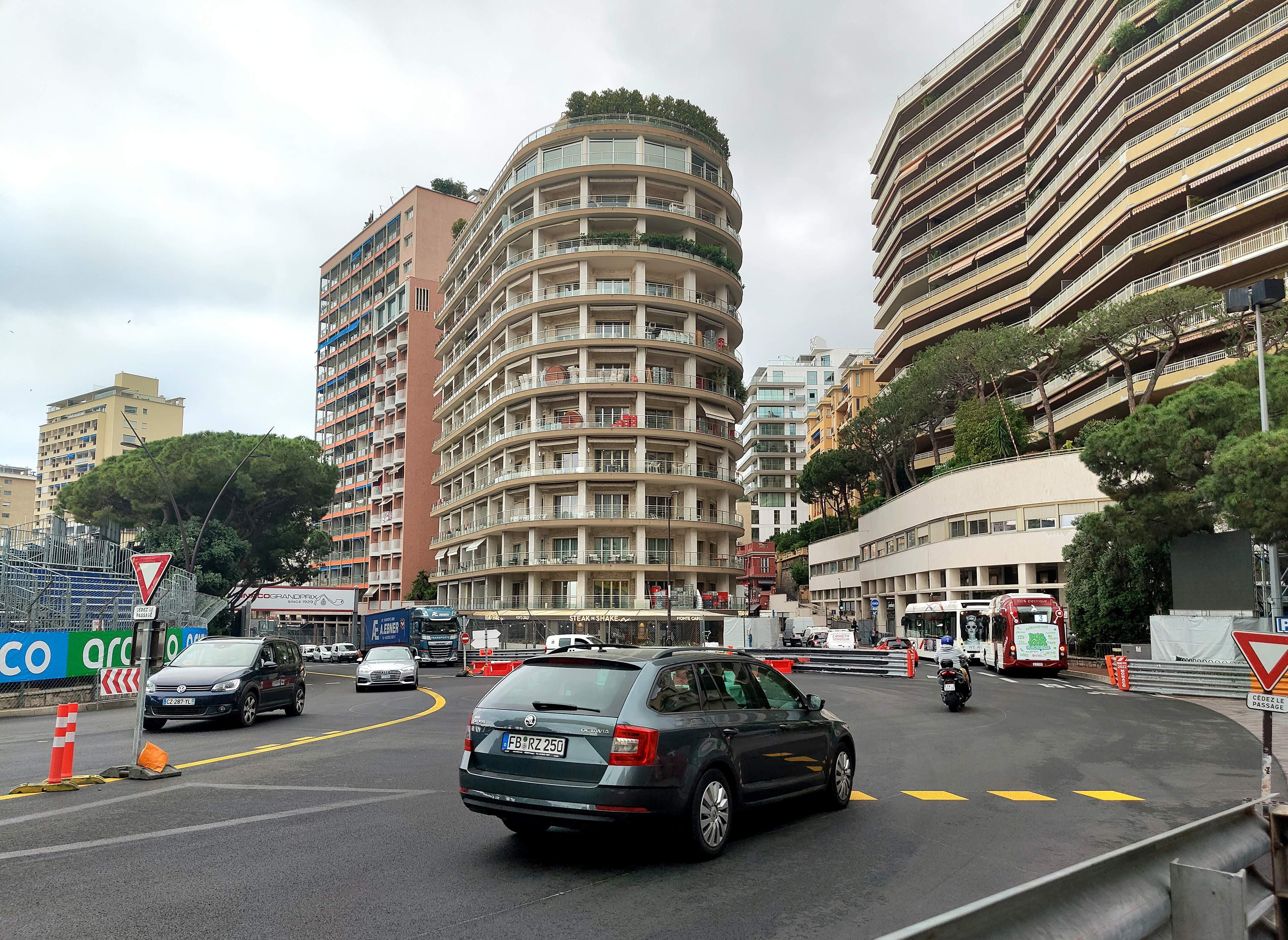 Cars and a bus driving round the Sainte-Dévote corner in Monaco, with the race barriers already in place