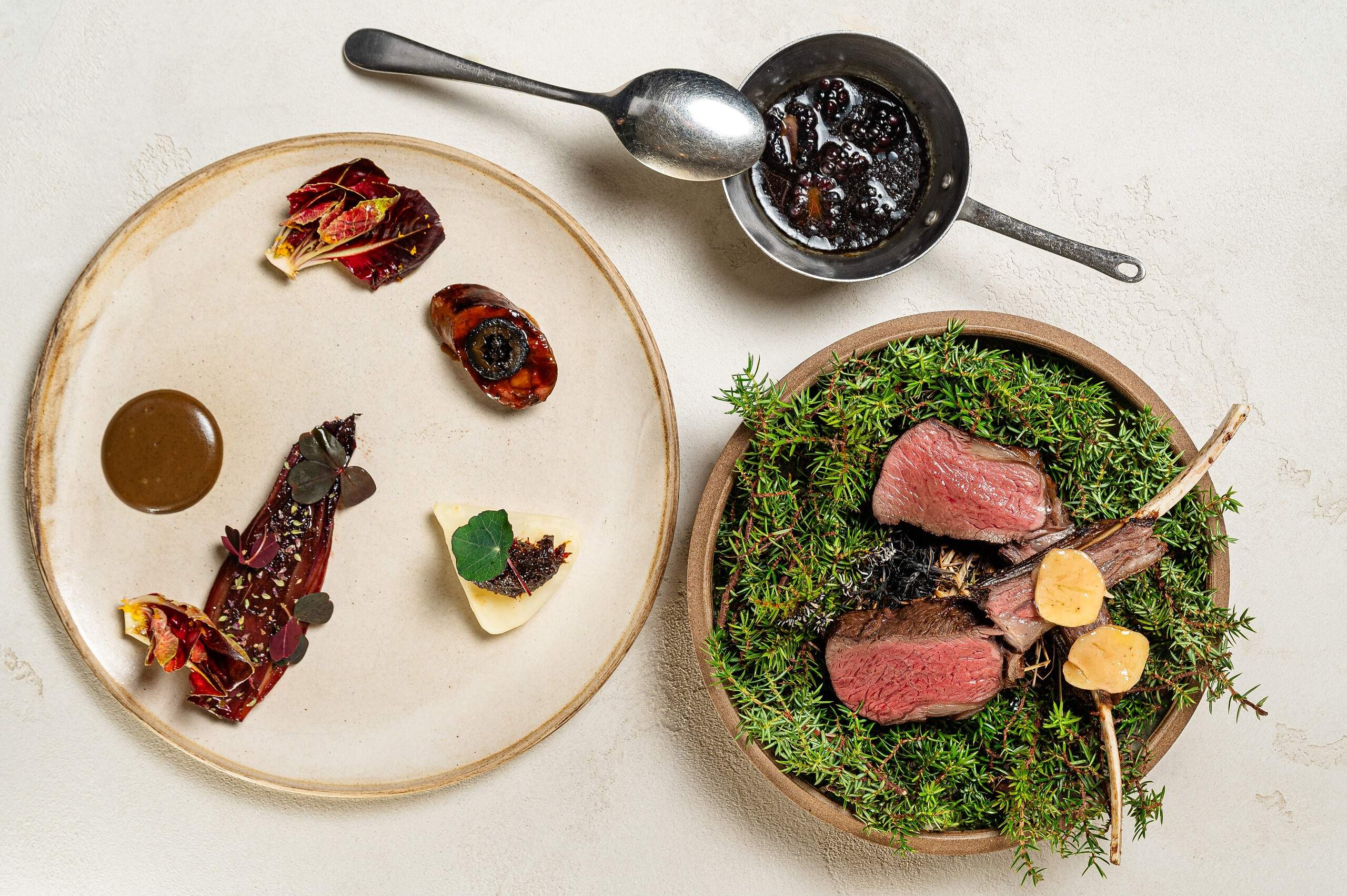 Venison on a bed of herbs beside a plate of small courses at HIDE