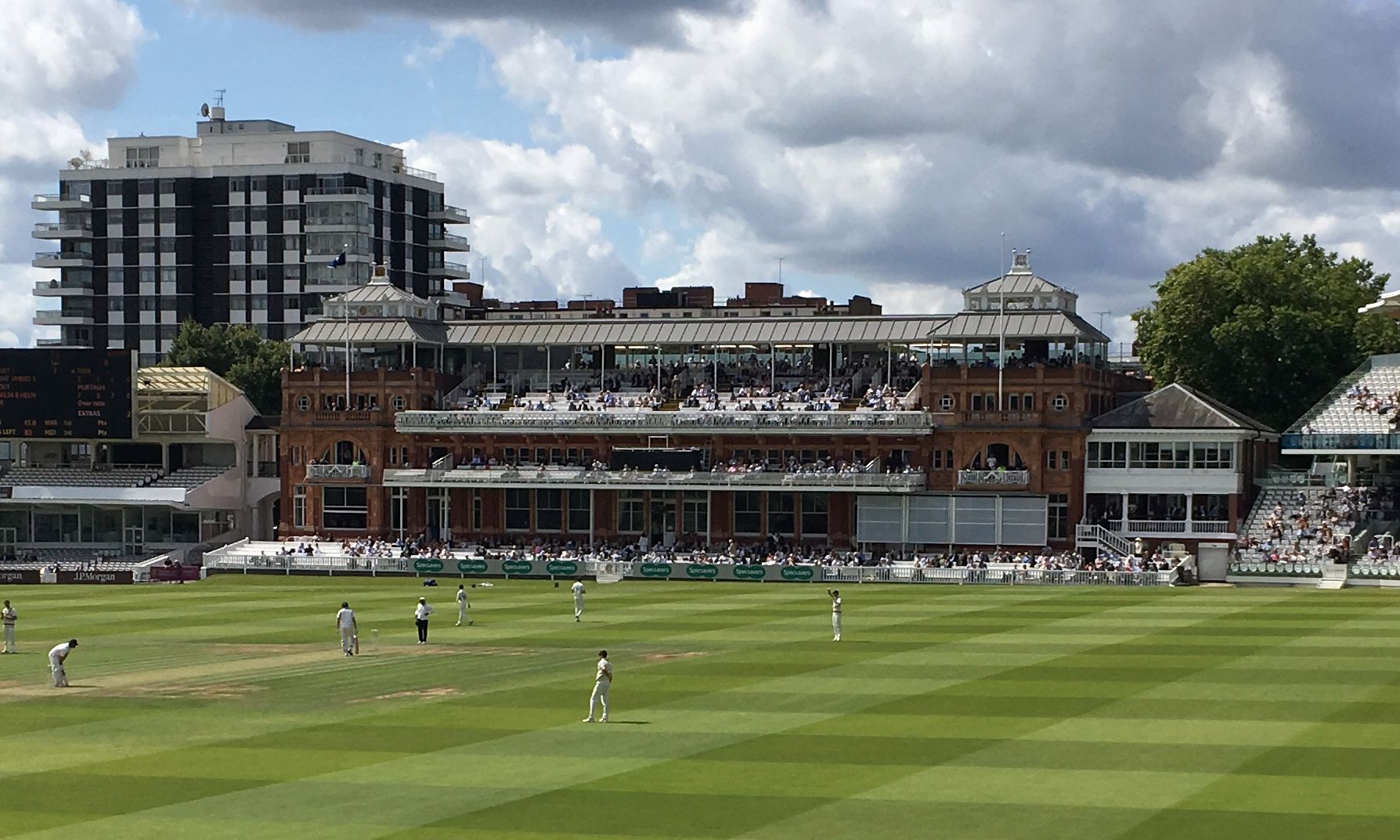 The Pavilion at Lord’s seen from across the ground during play, its balconies filled with spectators, with open seating stands on either side