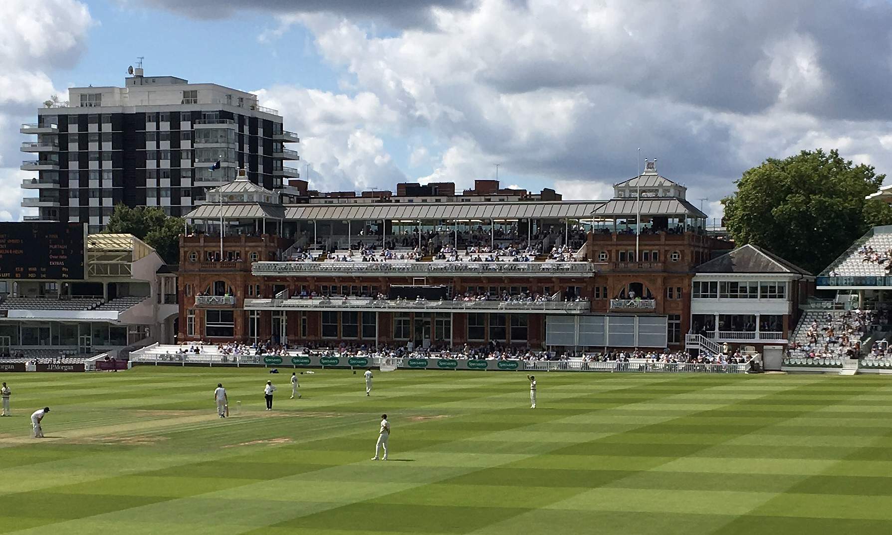 The Pavilion at Lord’s seen from across the ground during play, its balconies filled with spectators, with open seating stands on either side