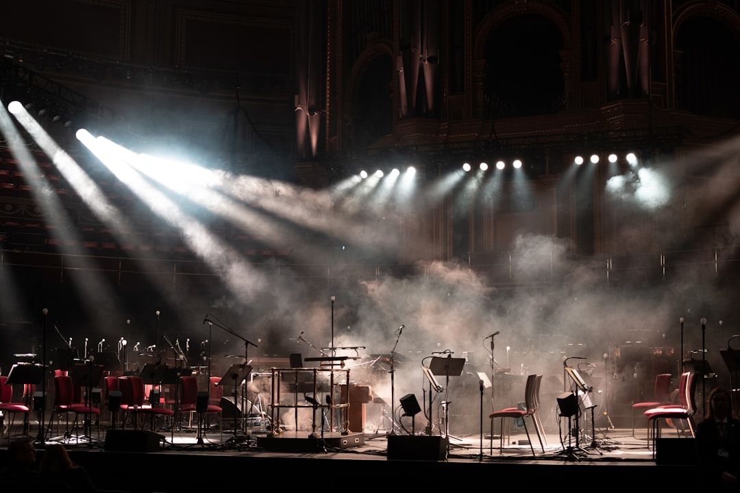 Orchestra performing on stage with spotlights and atmospheric lighting at a grand venue