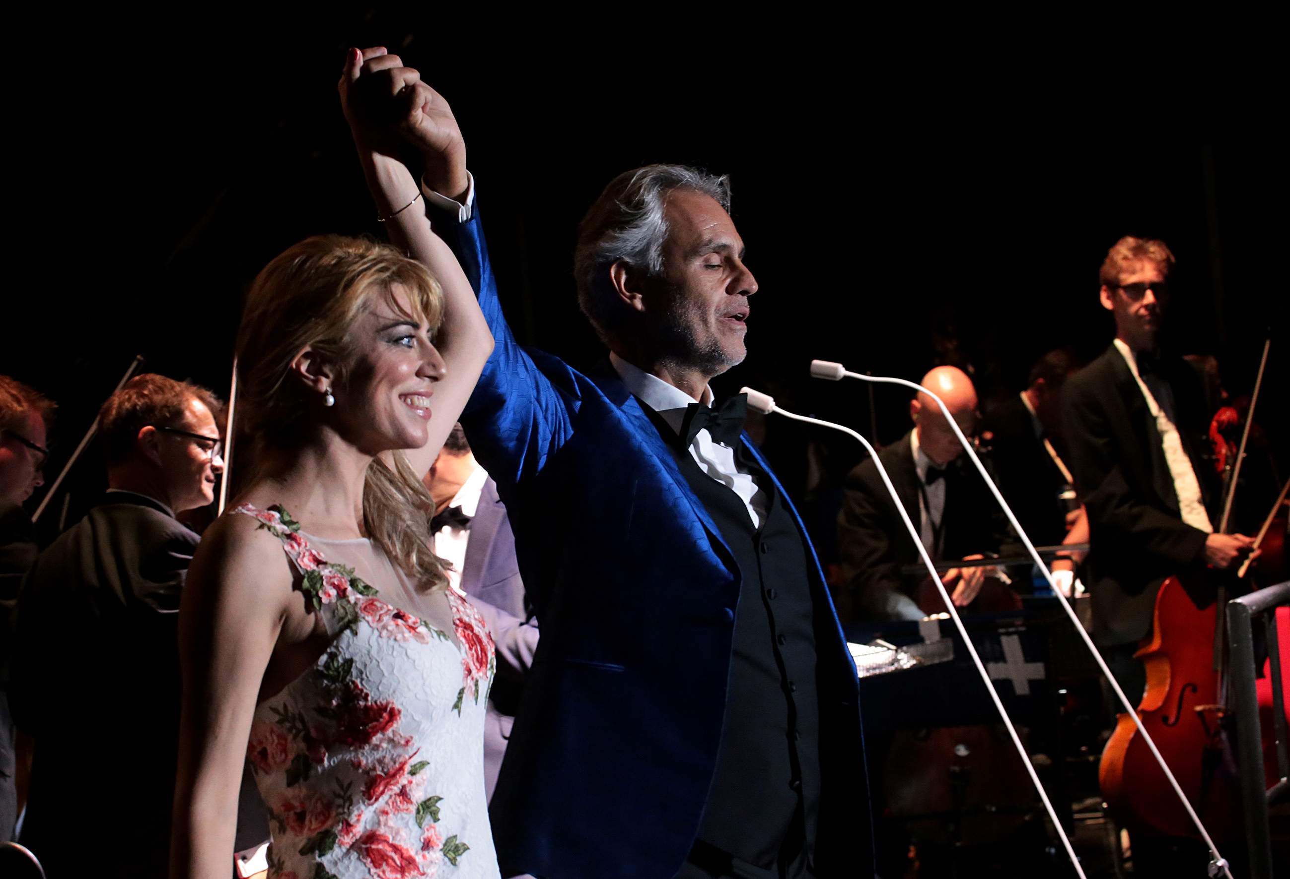Andrea Bocelli taking a bow beside a soprano, arms raised