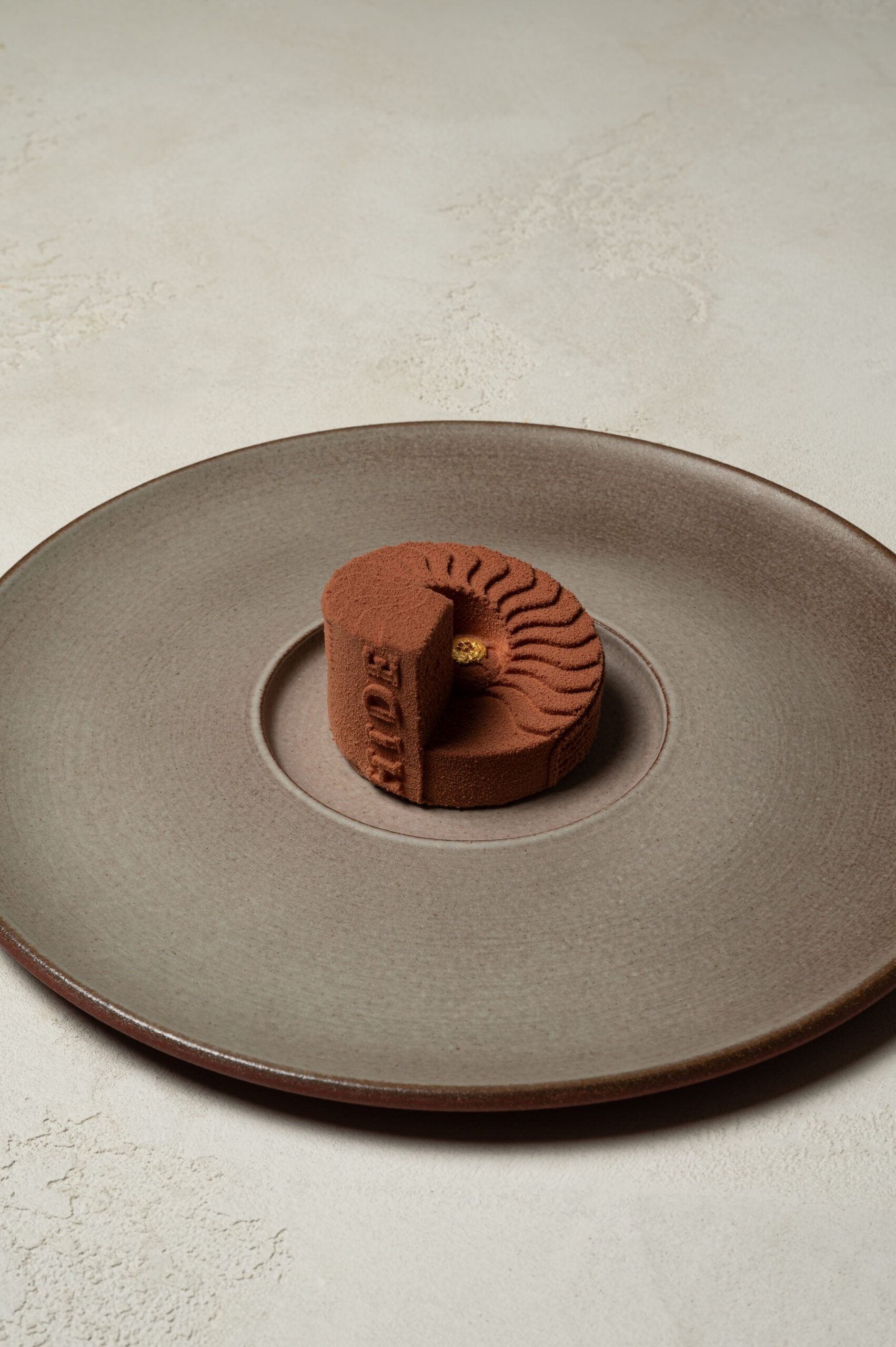 A chocolate dessert at HIDE, sculpted like the restaurant's spiral oak staircase and stamped with its name, on a wide grey plate
