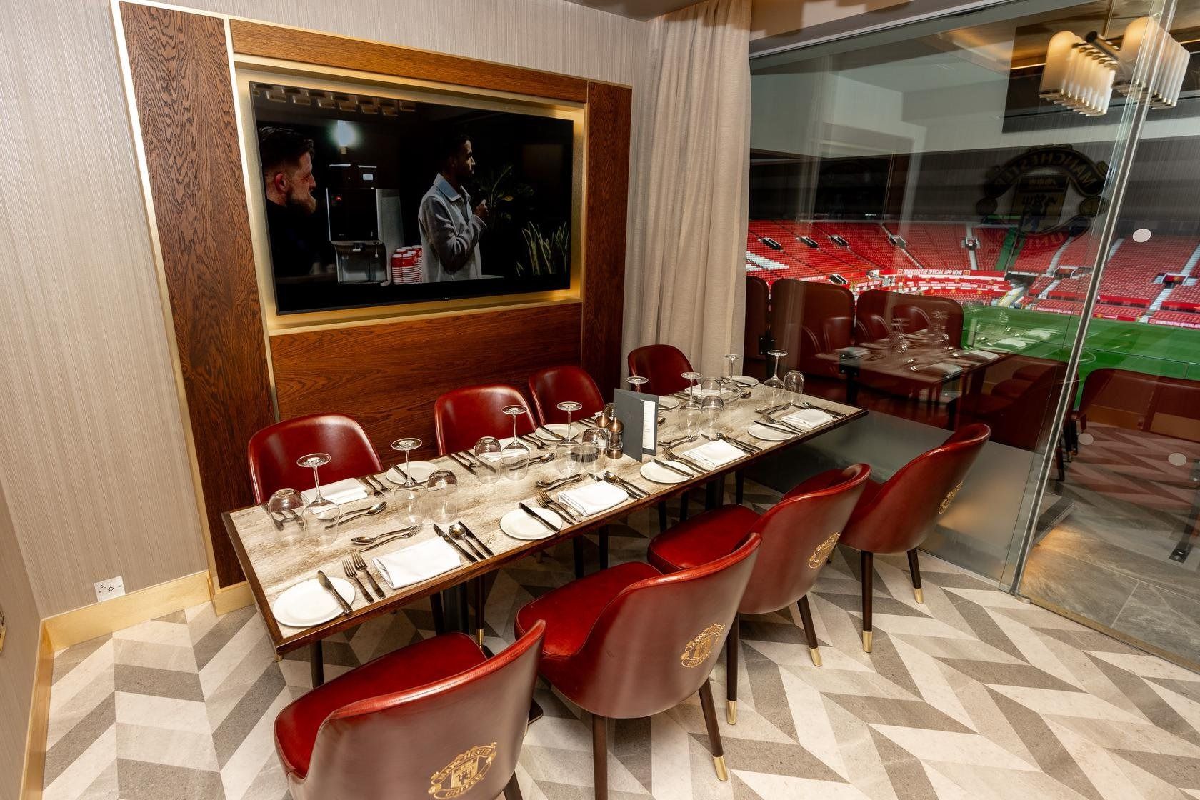 A private dining box with crested leather chairs and a marble table looking onto the pitch at Old Trafford