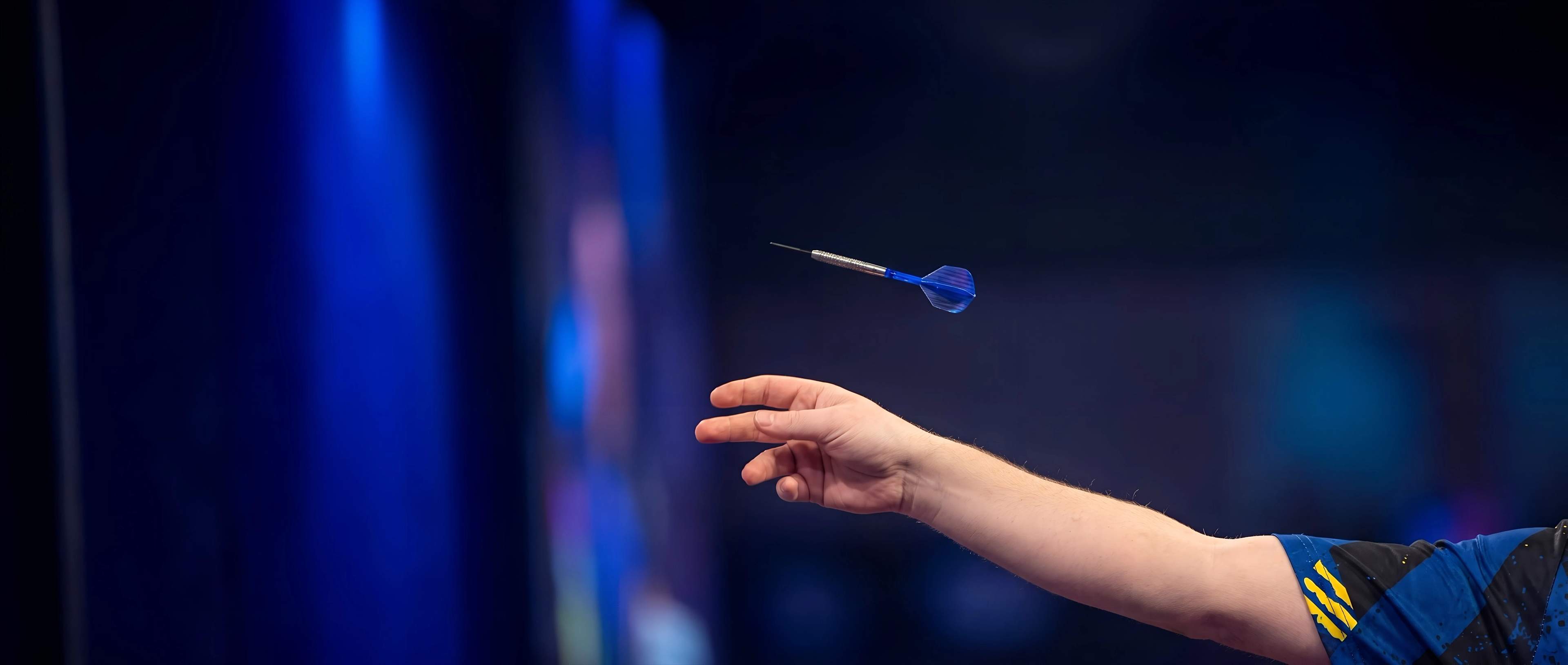 A darts player's hand at the moment of release, the dart in flight on stage