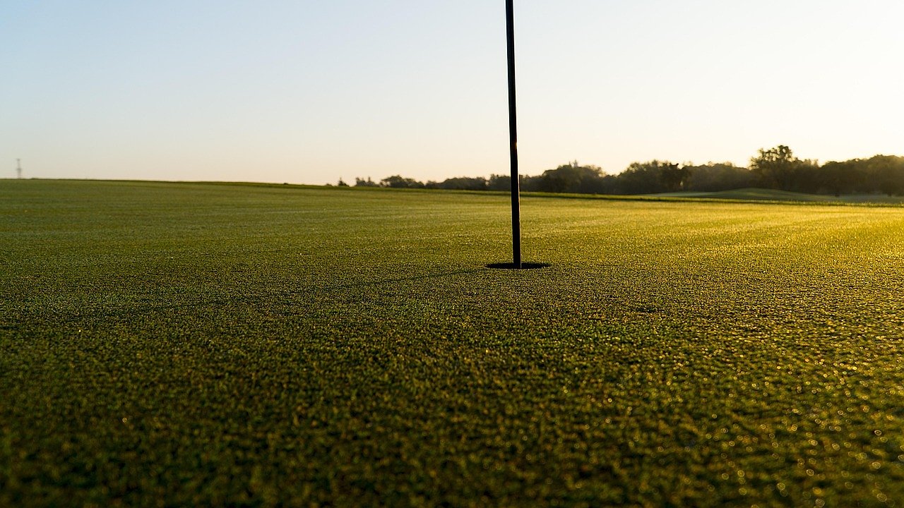 Golfers on a lush green golf course with rolling landscape