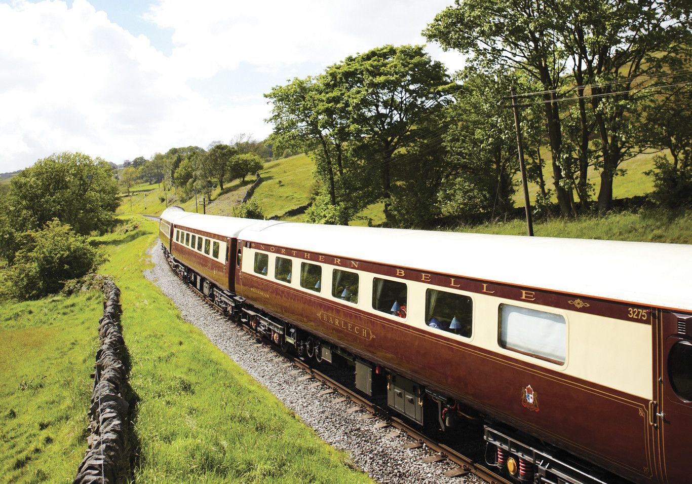The Northern Belle heritage carriages curving through green British countryside past a dry-stone wall