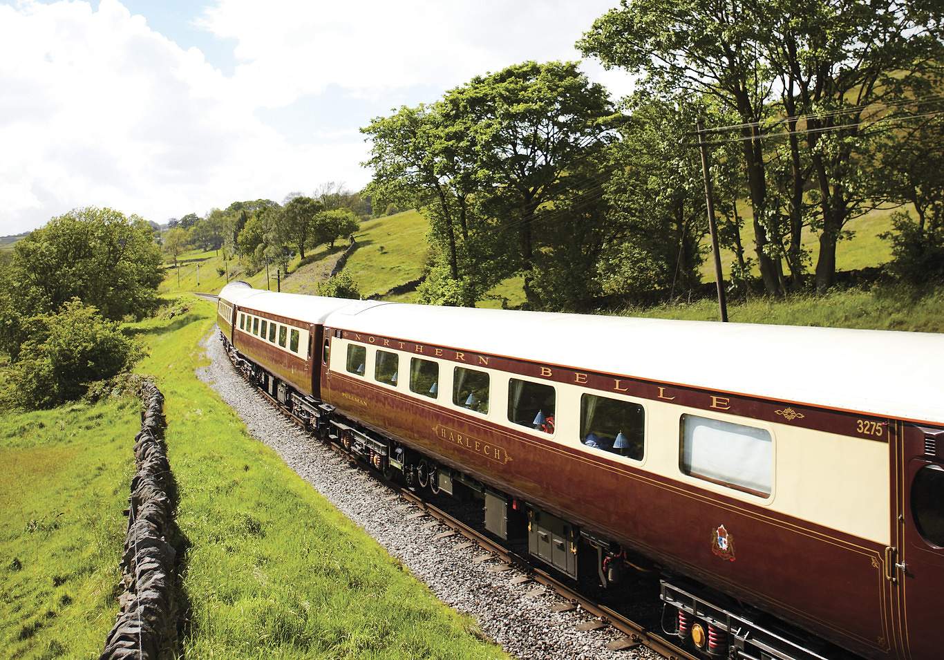 The Northern Belle heritage carriages curving through green British countryside past a dry-stone wall