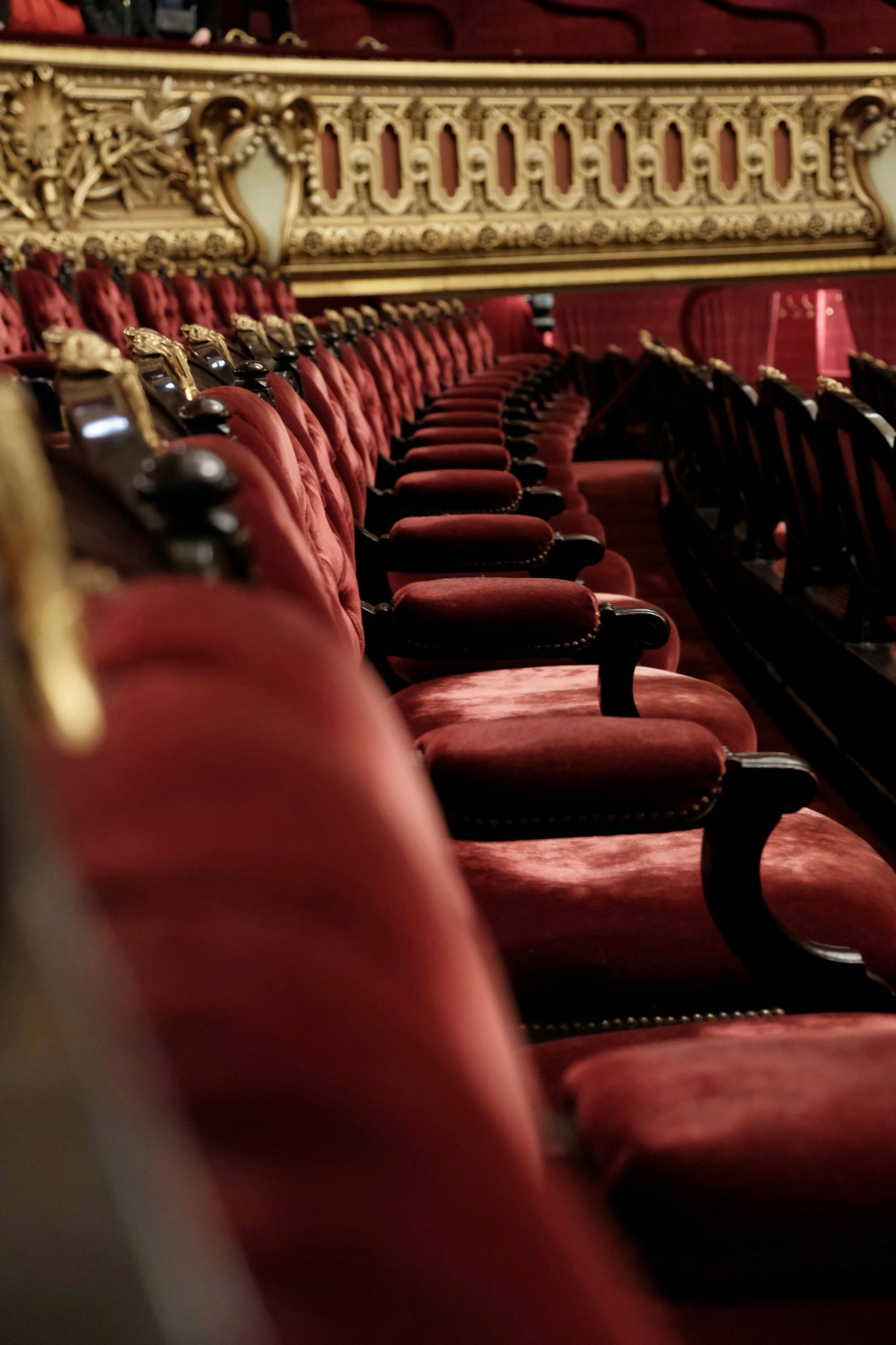A row of red velvet theatre seats beneath a gilded balcony front
