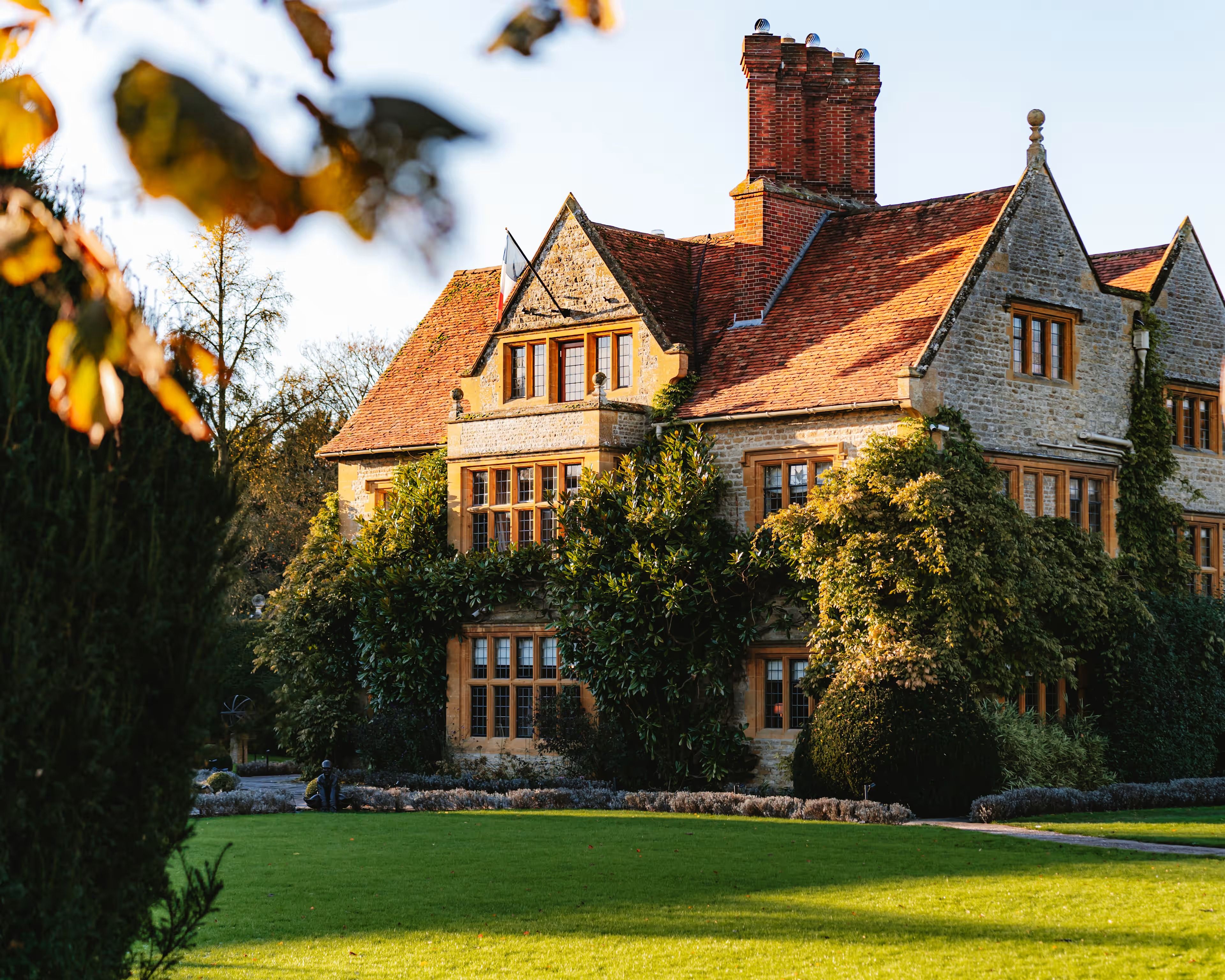 The stone manor house at Le Manoir aux Quat’Saisons in low autumn sun across the lawn