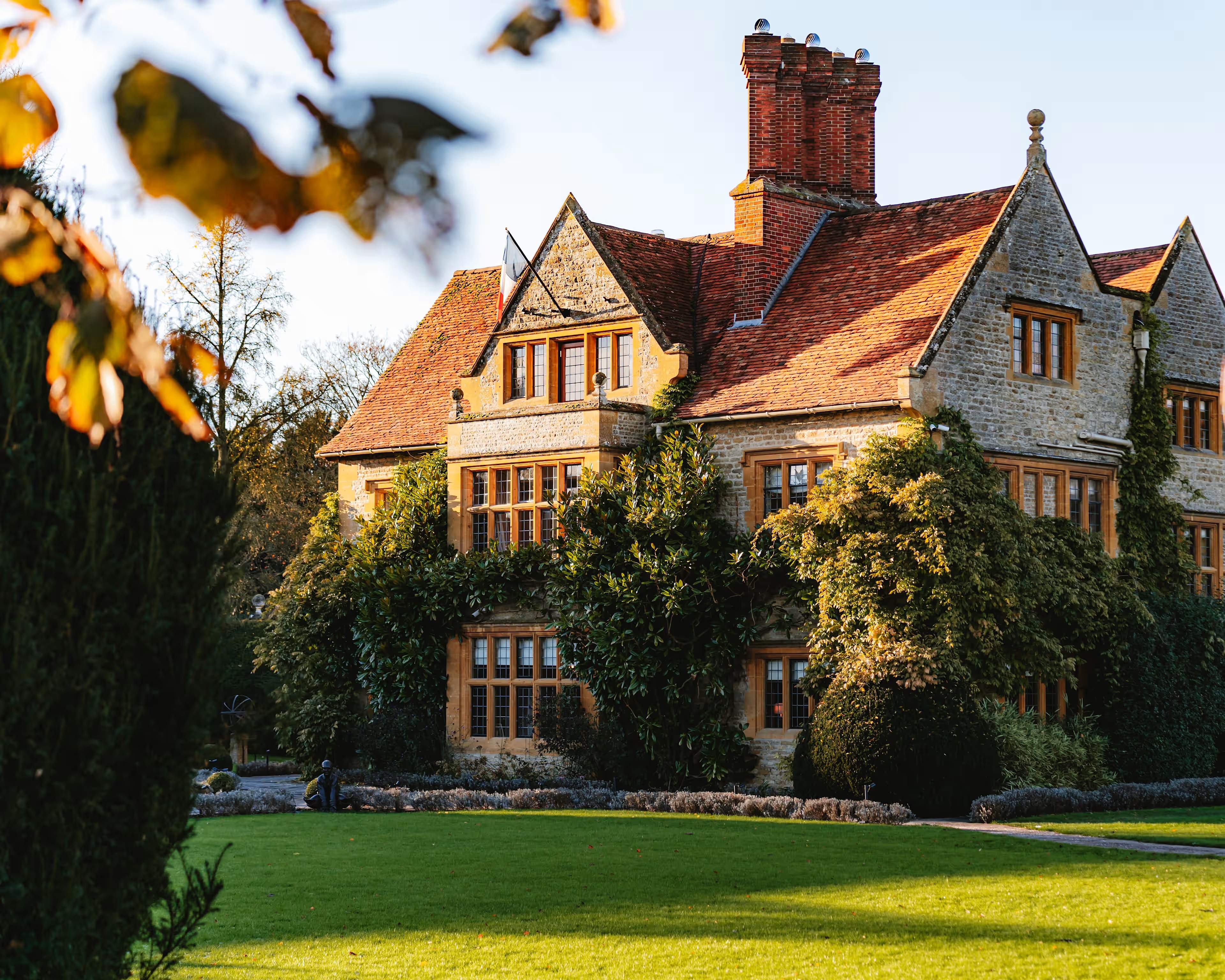 The stone manor house at Le Manoir aux Quat’Saisons in low autumn sun across the lawn