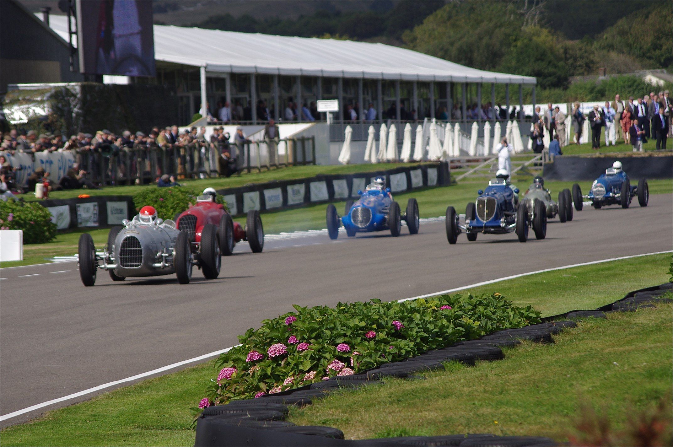 Pre-war Grand Prix cars racing on the Goodwood Motor Circuit at the Revival with a period crowd behind